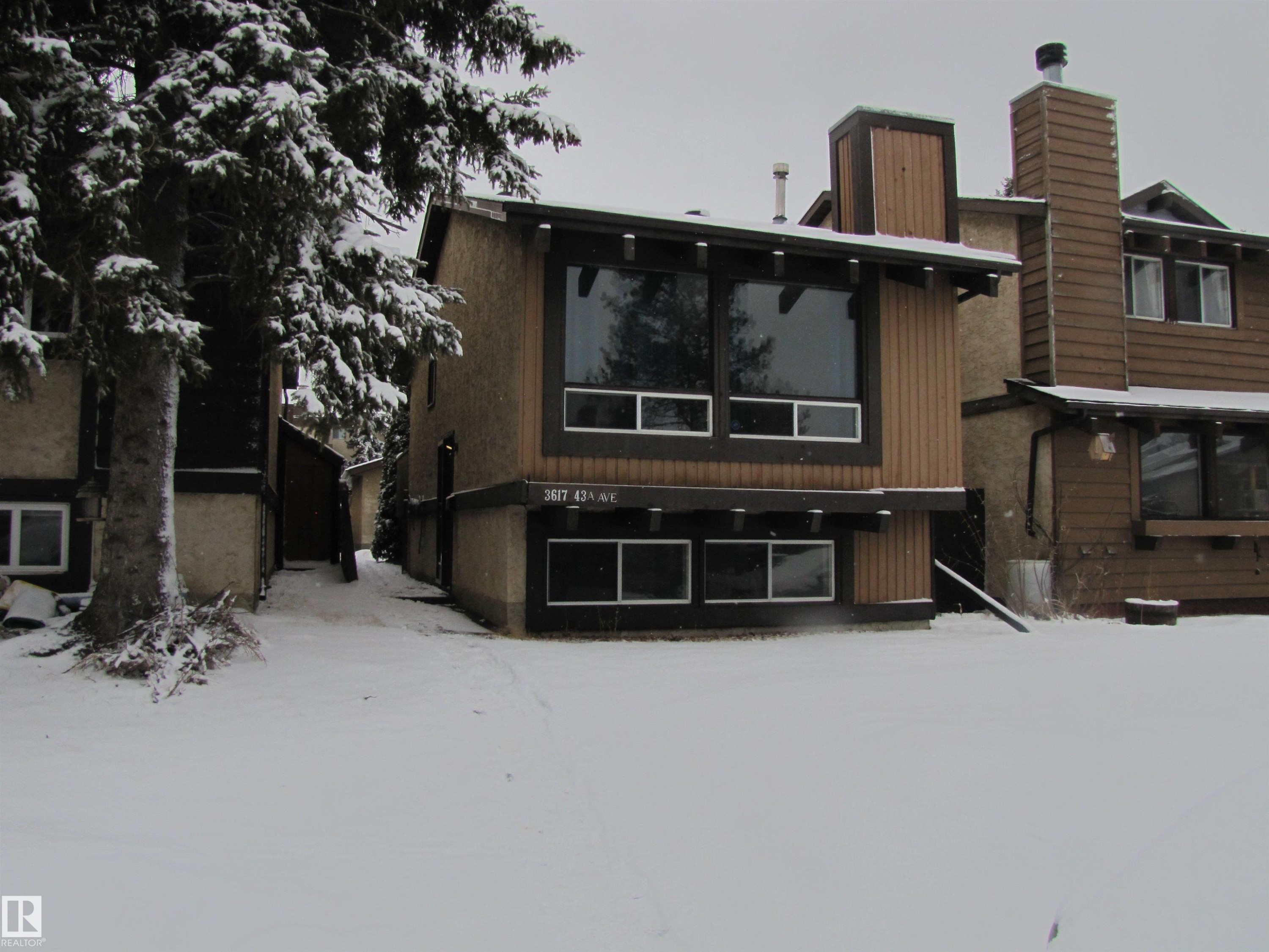 The property features an exterior with light brown stucco and dark brown siding, large windows, and a prominent chimney - 3617 43A Avenue, Edmonton, AB - Outdoor