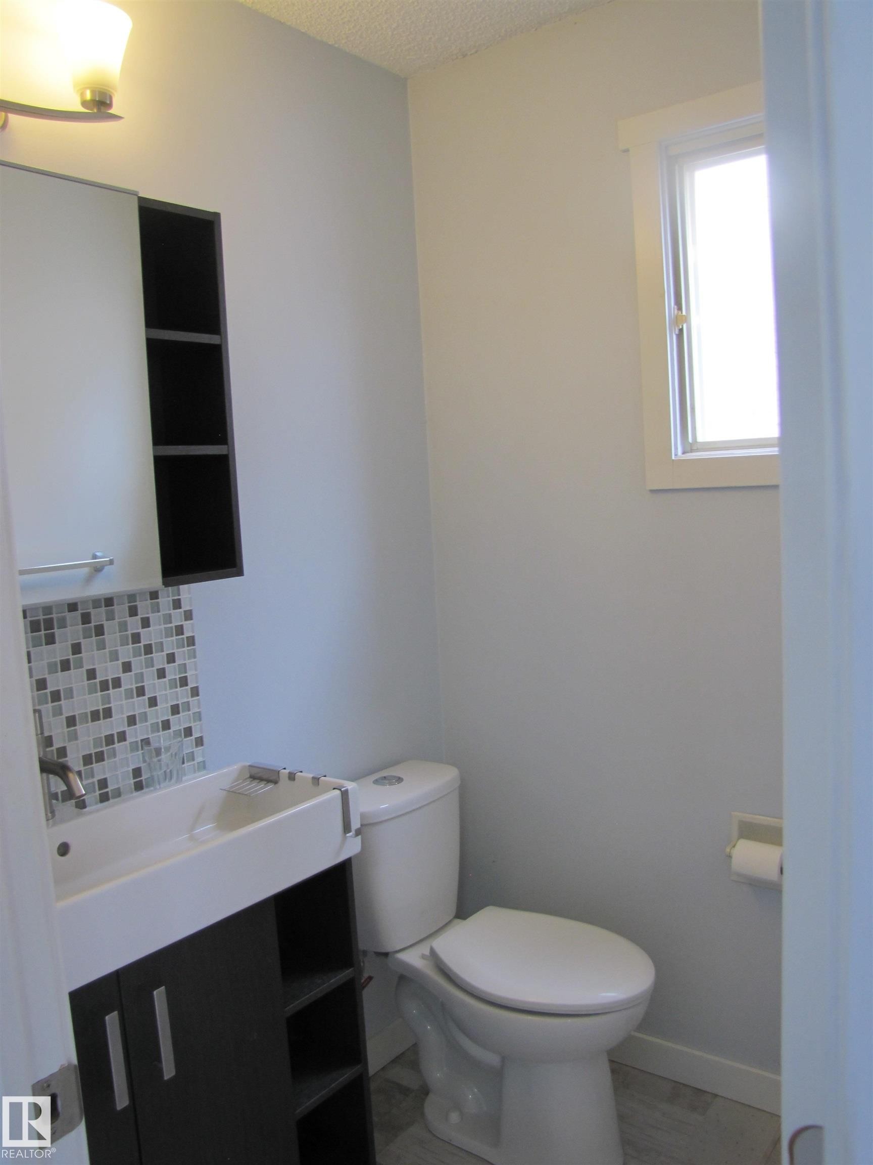 The bathroom features a modern vanity with a white rectangular sink, a mosaic tile backsplash, and a window for natural light - 3617 43A Avenue, Edmonton, AB - Indoor Photo Showing Bathroom