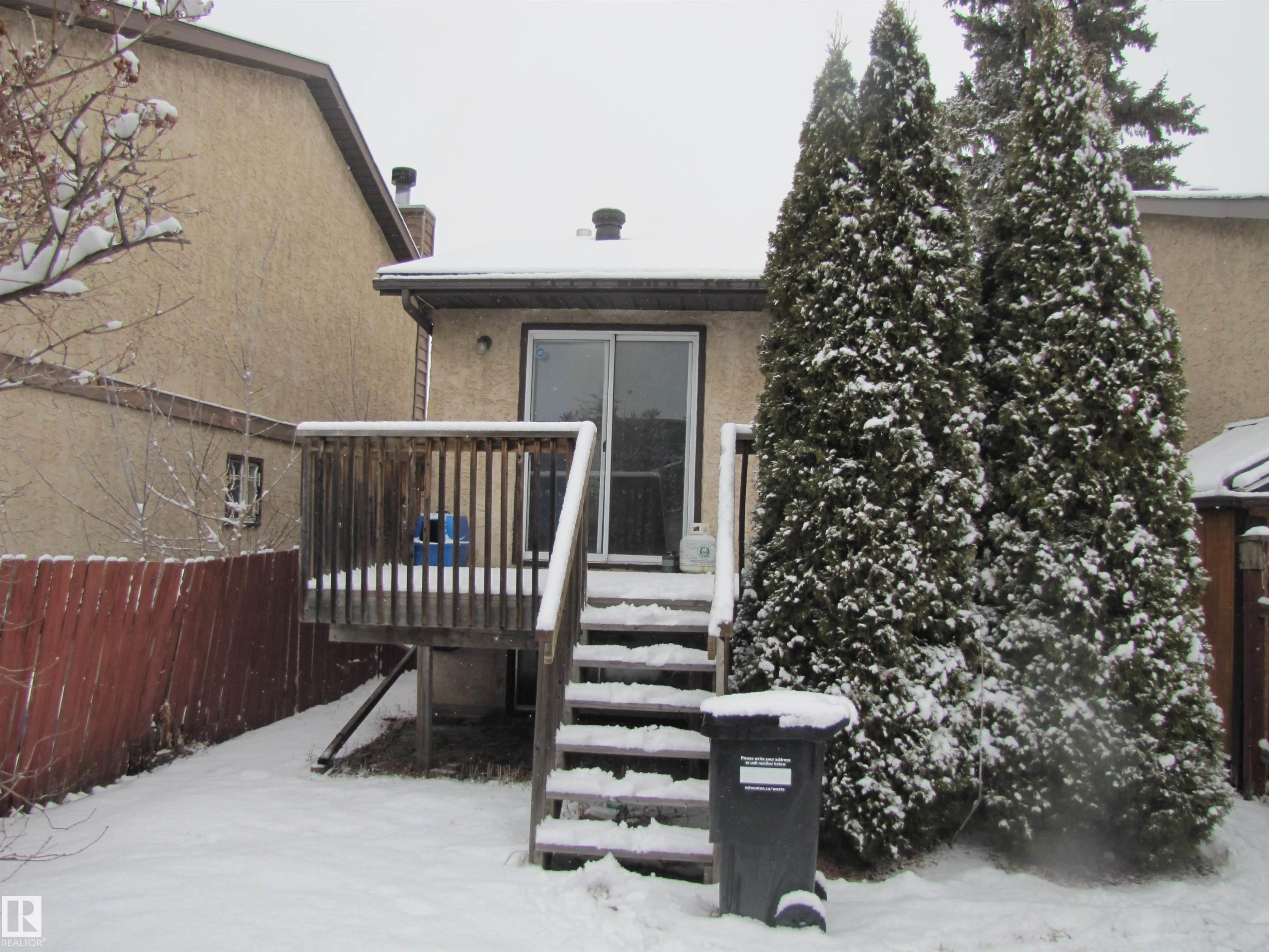 The property features a wooden deck with railing and stairs, leading to a sliding glass door - 3617 43A Avenue, Edmonton, AB - Outdoor