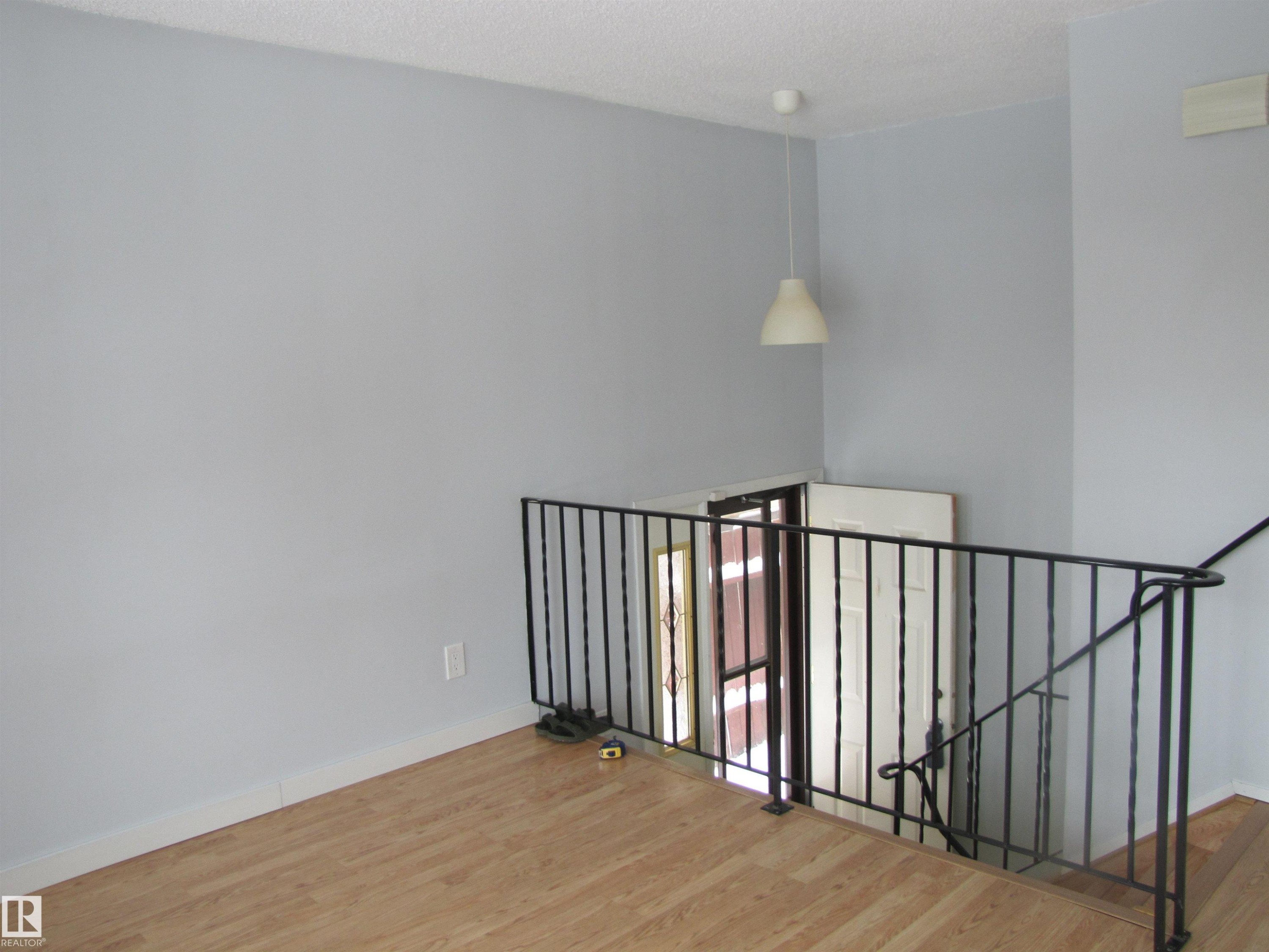 Open space featuring light-toned flooring, a black metal railing, and a white pendant light fixture - 3617 43A Avenue, Edmonton, AB - Indoor Photo Showing Other Room
