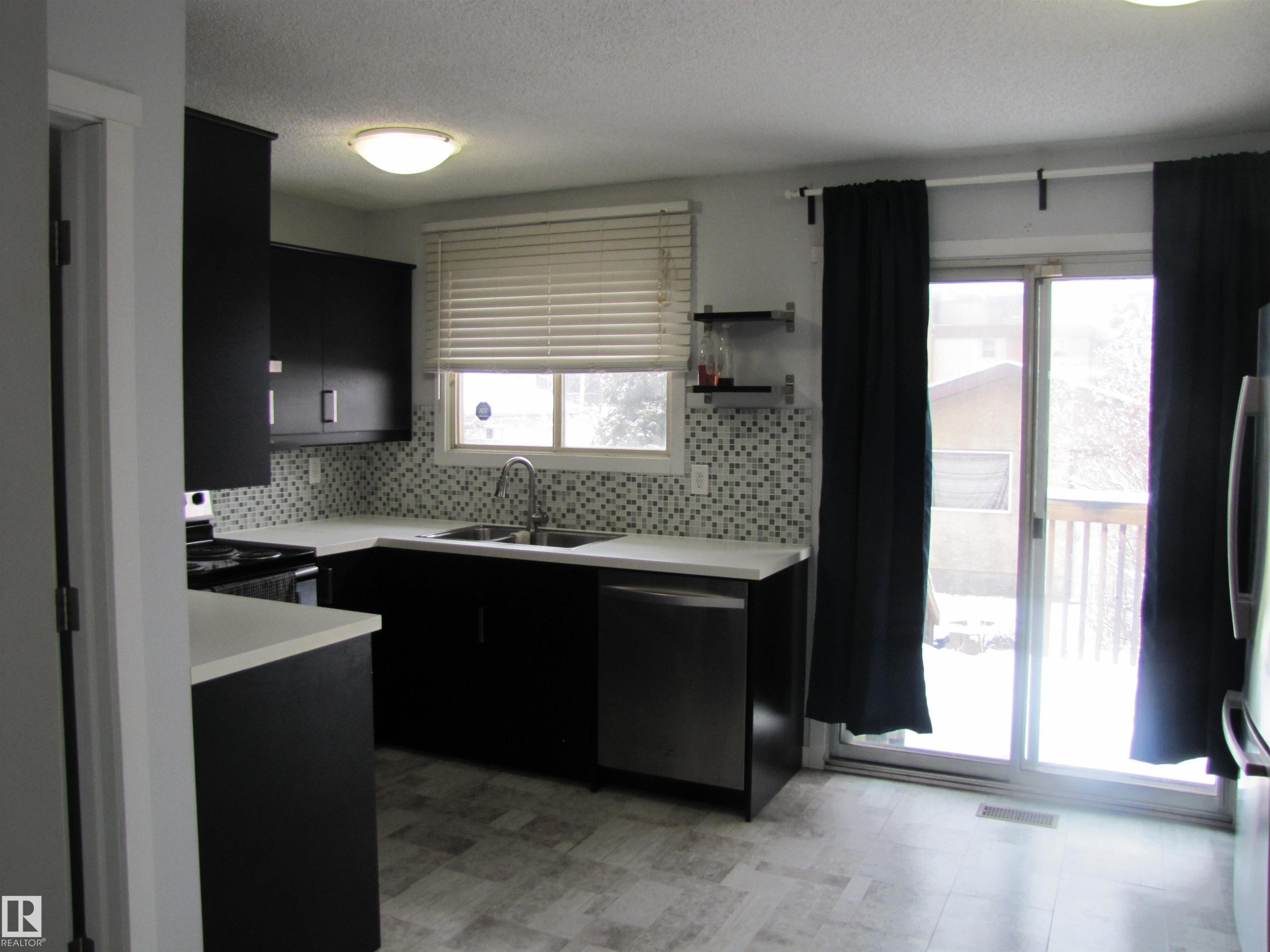 The kitchen features dark cabinetry, light countertops, and a mosaic tile backsplash - 3617 43A Avenue, Edmonton, AB - Indoor Photo Showing Kitchen With Upgraded Kitchen