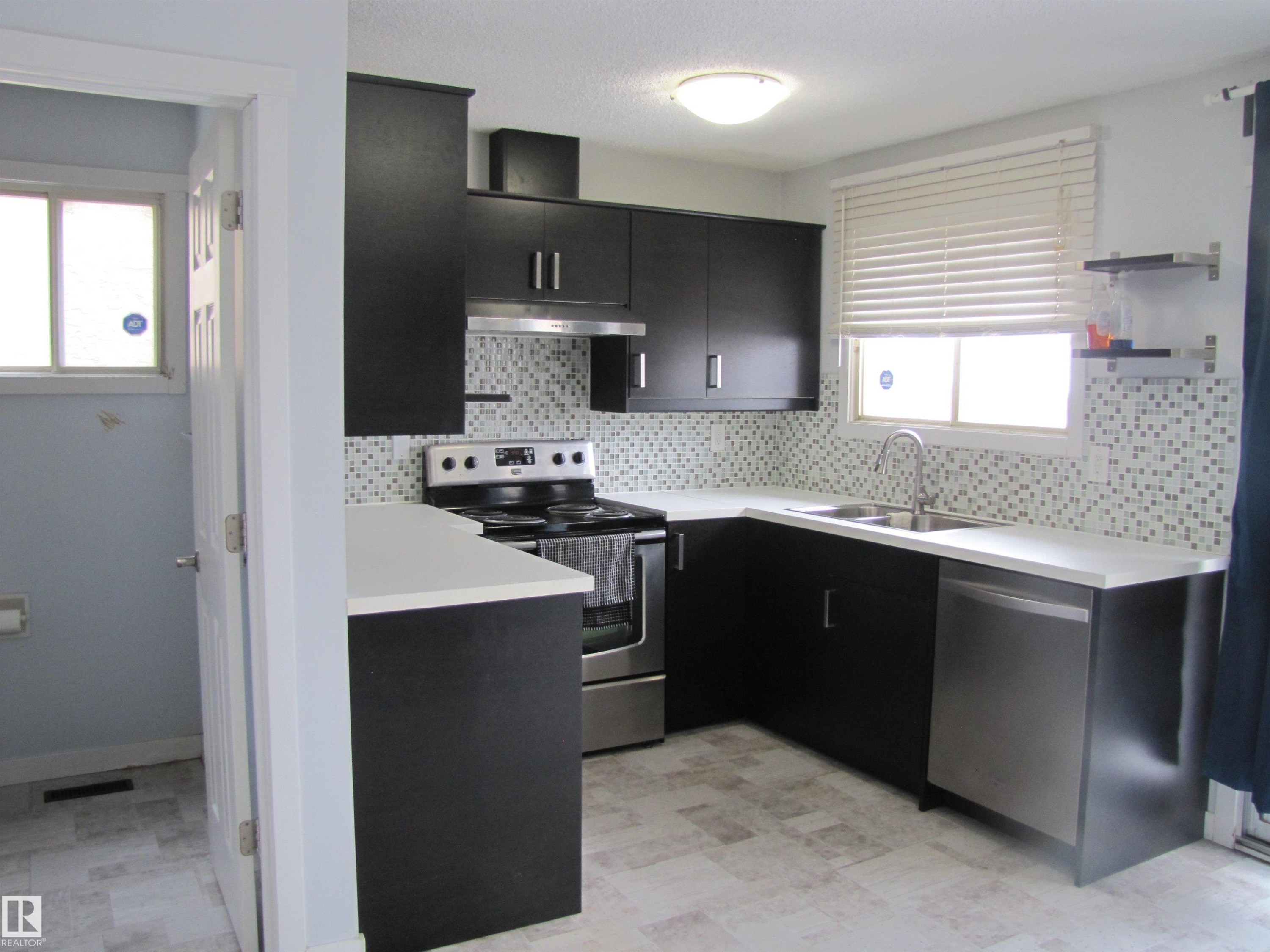 The kitchen features dark cabinetry, light countertops, and a mosaic tile backsplash - 3617 43A Avenue, Edmonton, AB - Indoor Photo Showing Kitchen With Stainless Steel Kitchen With Double Sink With Upgraded Kitchen