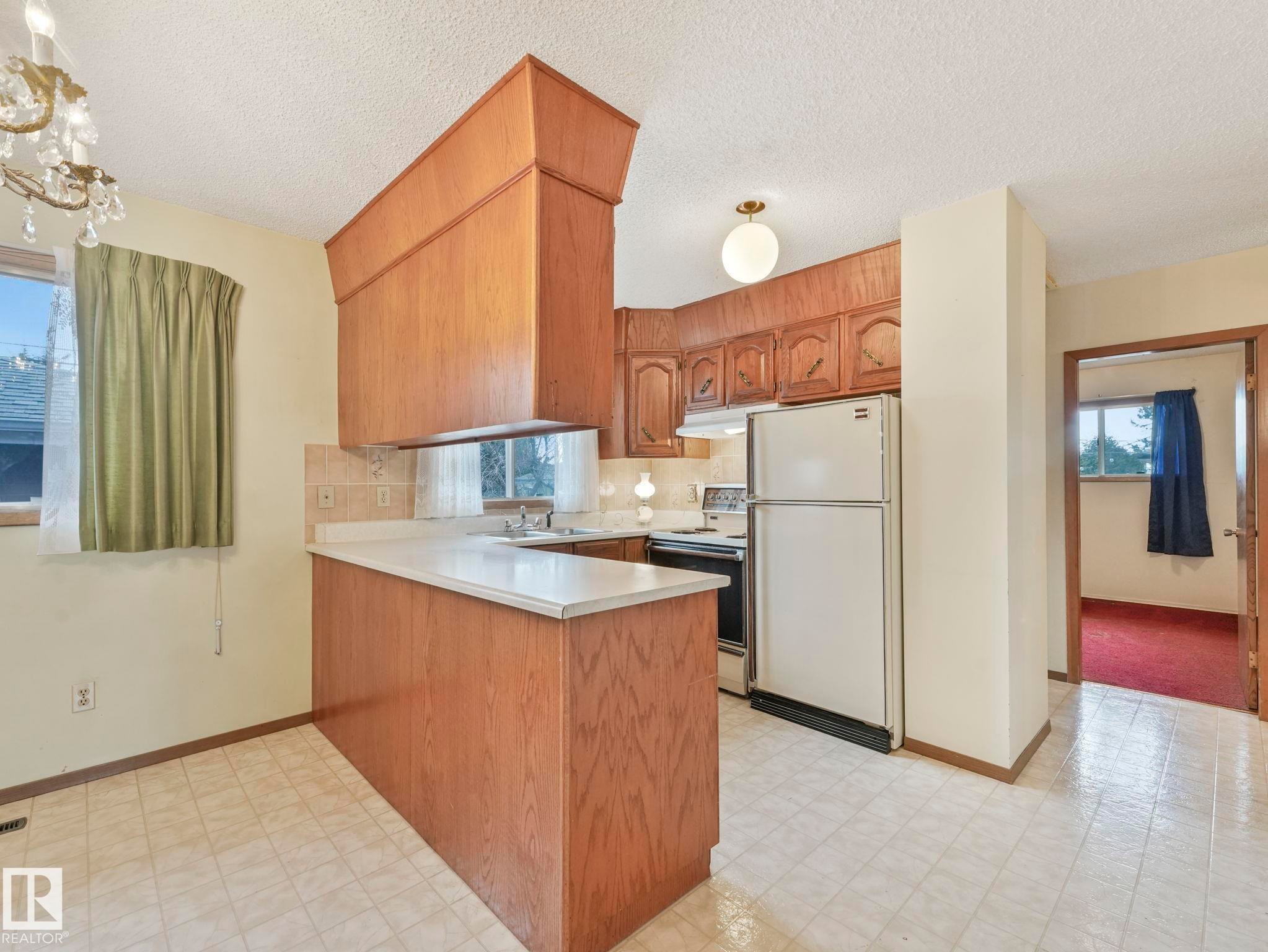 Kitchen featuring wood cabinetry, a white refrigerator, a window with a curtain, and tiled flooring - 5904 84 Avenue, Edmonton, AB - Indoor Photo Showing Kitchen