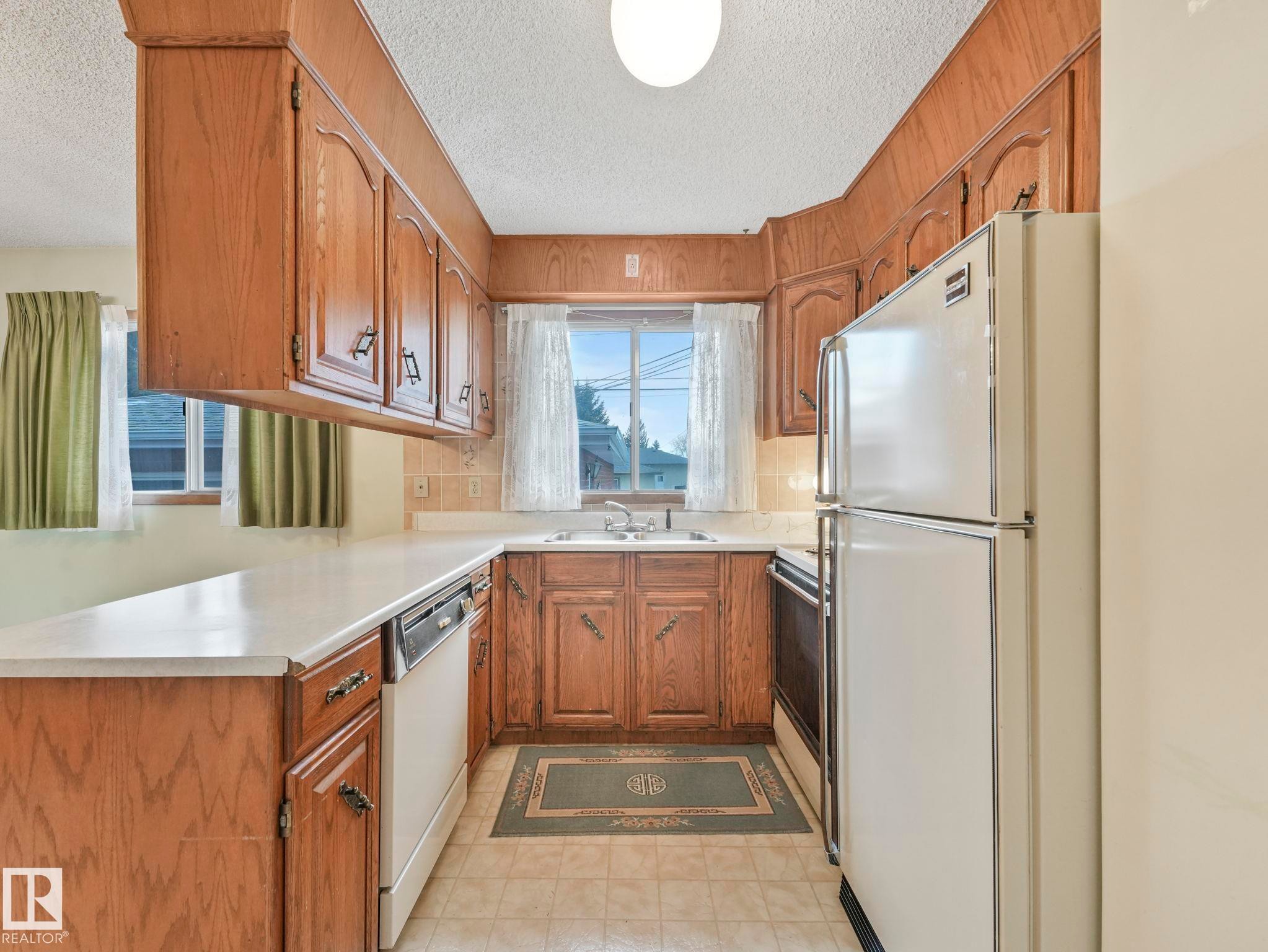 The kitchen features wood cabinetry, a double basin sink beneath a window, and a white refrigerator - 5904 84 Avenue, Edmonton, AB - Indoor Photo Showing Kitchen