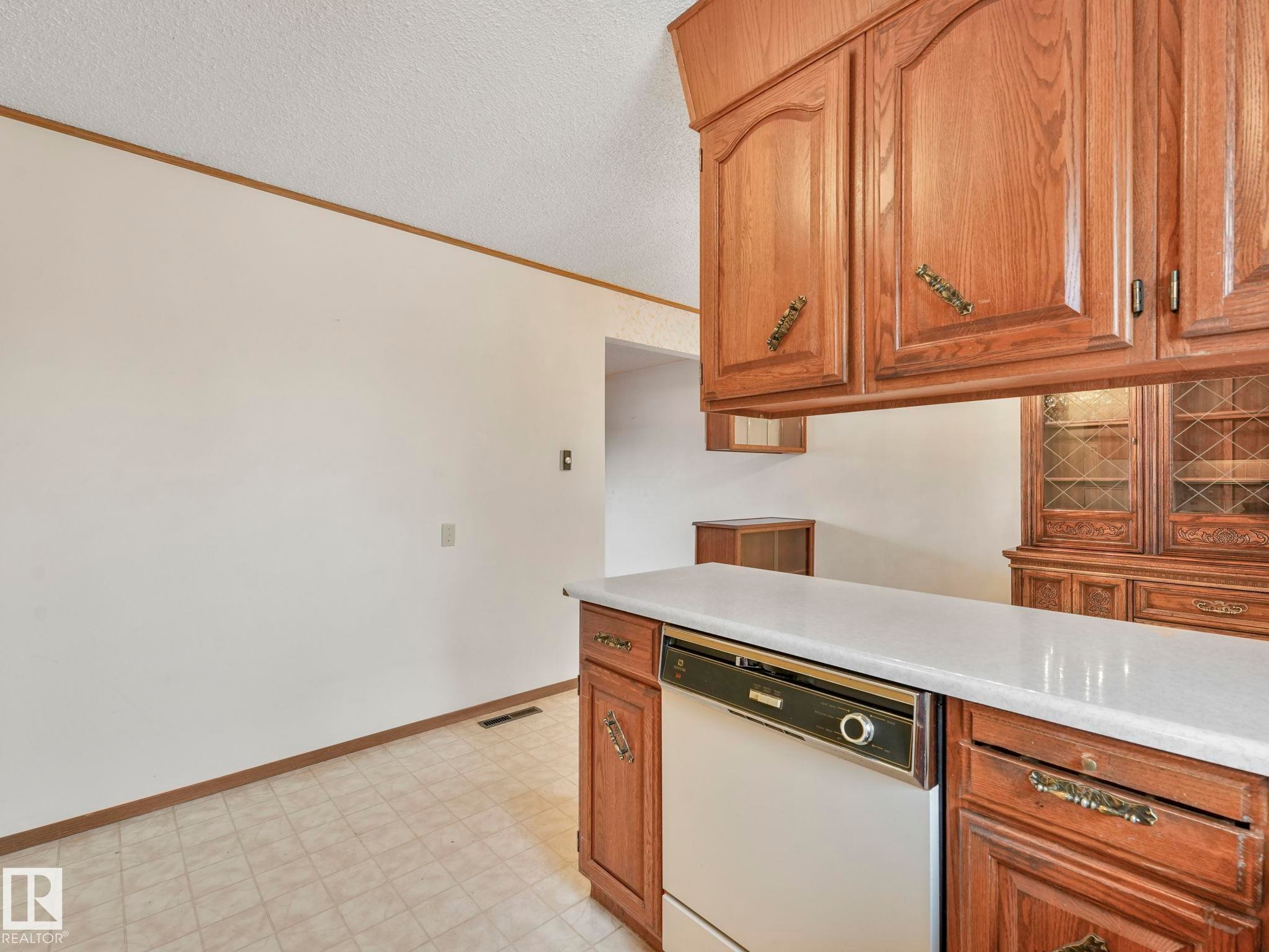 The kitchen features wood cabinetry, a white countertop, and a white dishwasher - 5904 84 Avenue, Edmonton, AB - Indoor Photo Showing Kitchen
