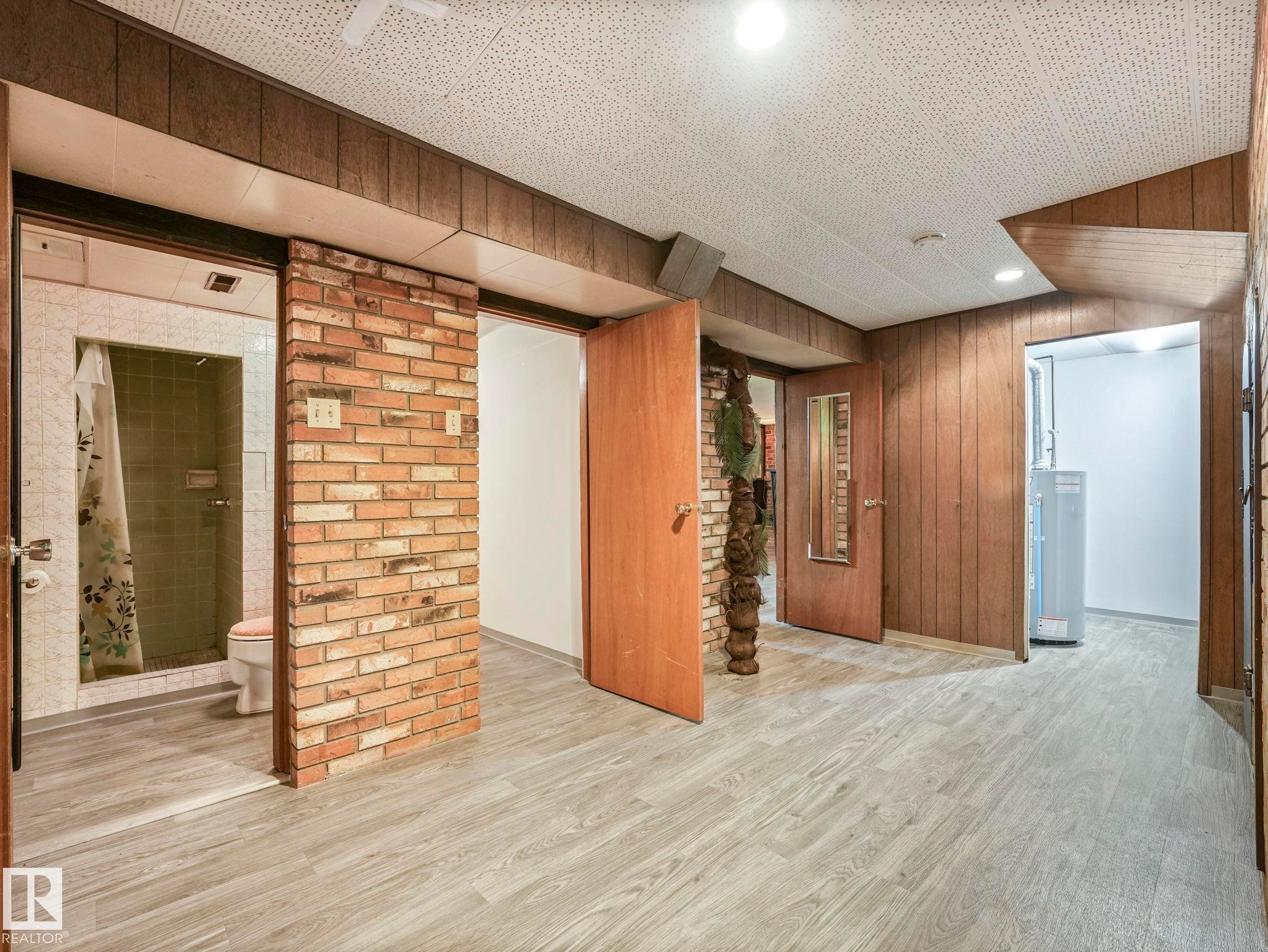 The property features wood paneling on the walls, a brick accent wall, and light-colored flooring - 5904 84 Avenue, Edmonton, AB - Indoor Photo Showing Other Room