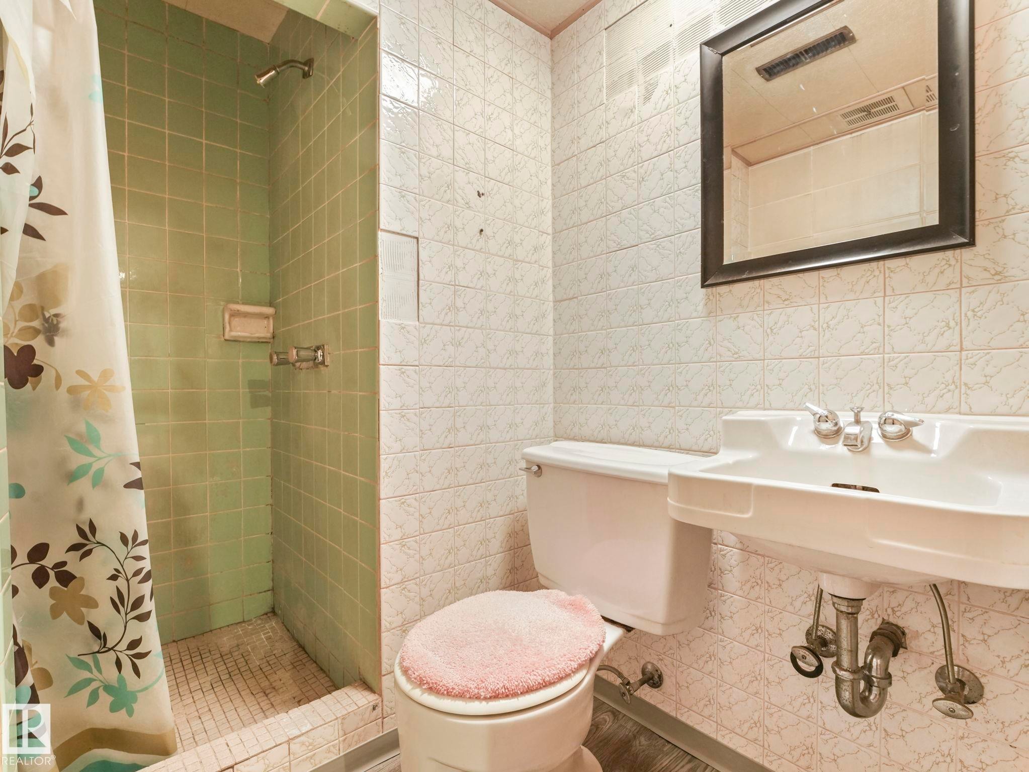 Bathroom featuring a shower with green tiled walls, a white sink with chrome fixtures, and a toilet - 5904 84 Avenue, Edmonton, AB - Indoor Photo Showing Bathroom