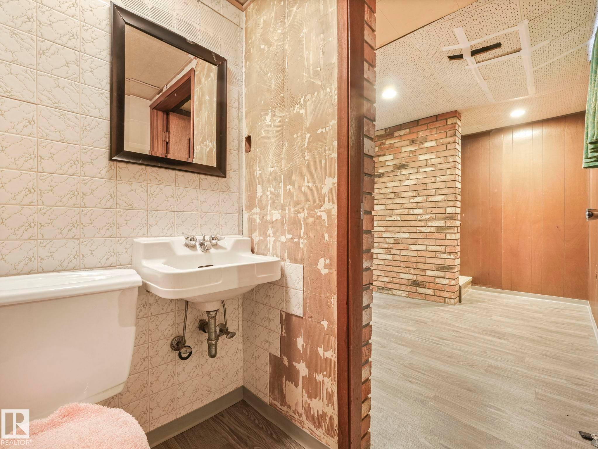 This area features a wall-mounted sink with a mirror above, set against a tiled wall - 5904 84 Avenue, Edmonton, AB - Indoor Photo Showing Bathroom