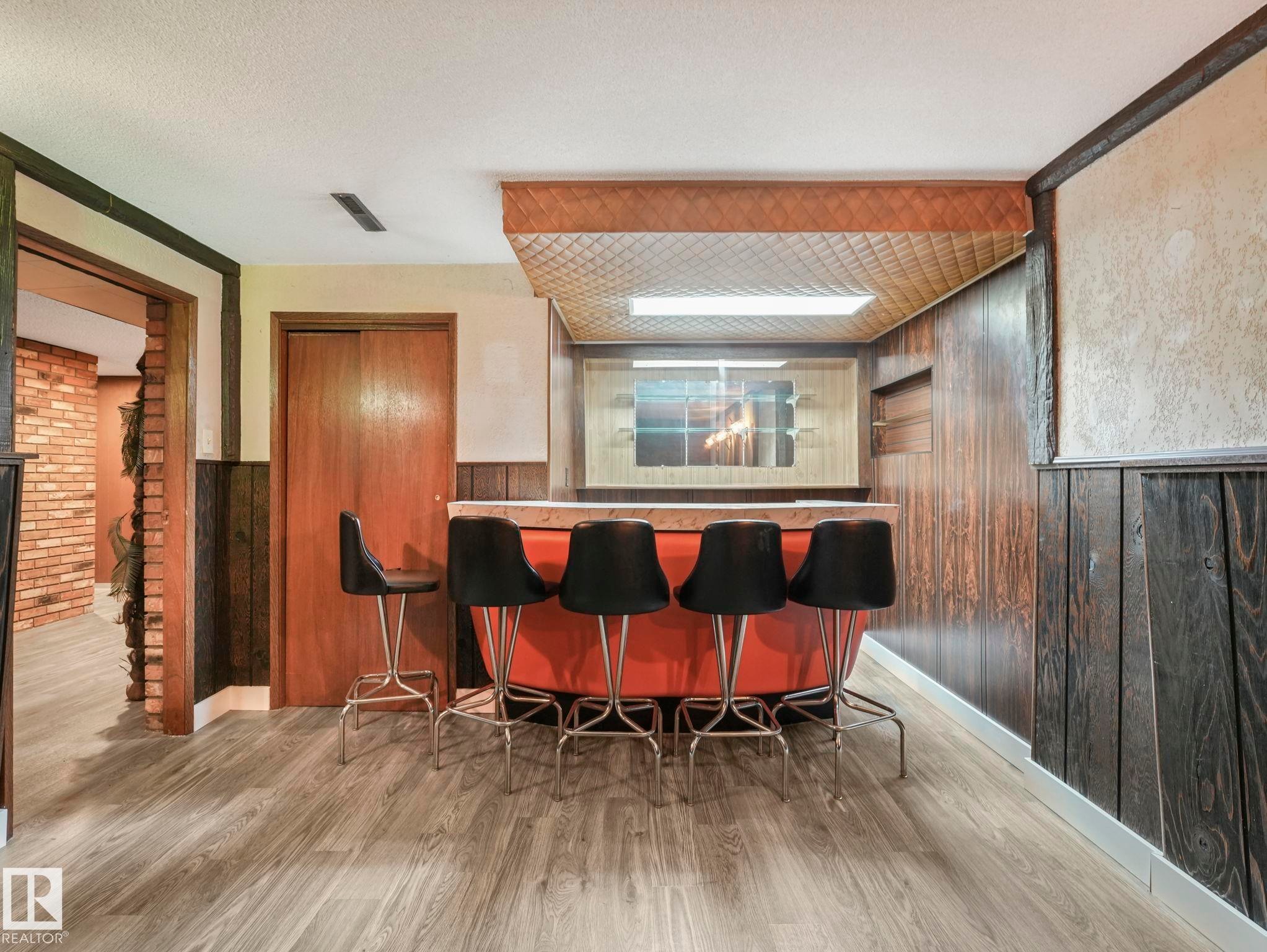 Living area featuring wood paneling, an integrated bar with a light-colored countertop, and light wood-style flooring - 5904 84 Avenue, Edmonton, AB - Indoor