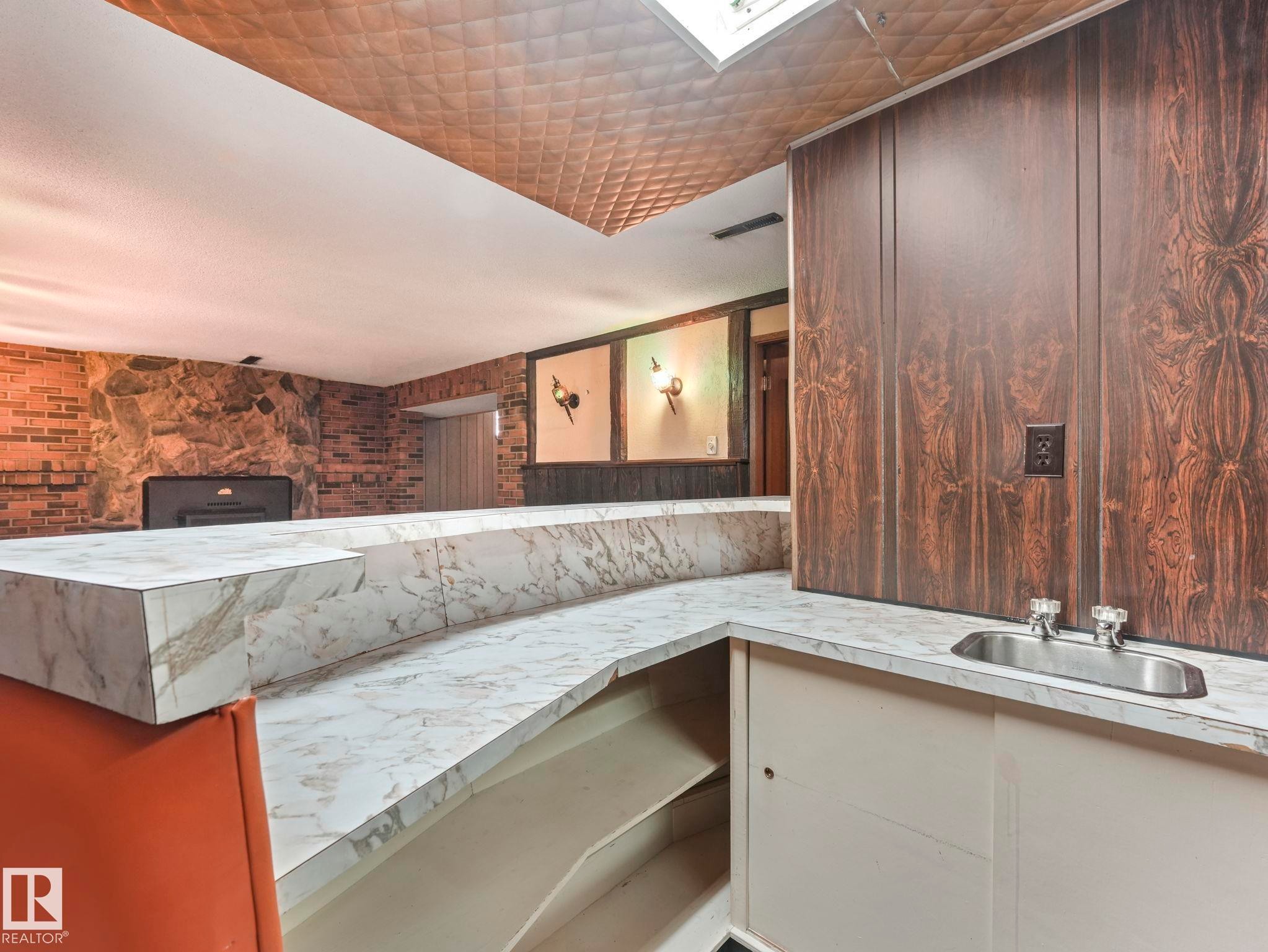 The property features a built-in bar with a countertop and an integrated sink, complemented by stone and brick wall finishes in the background - 5904 84 Avenue, Edmonton, AB - Indoor