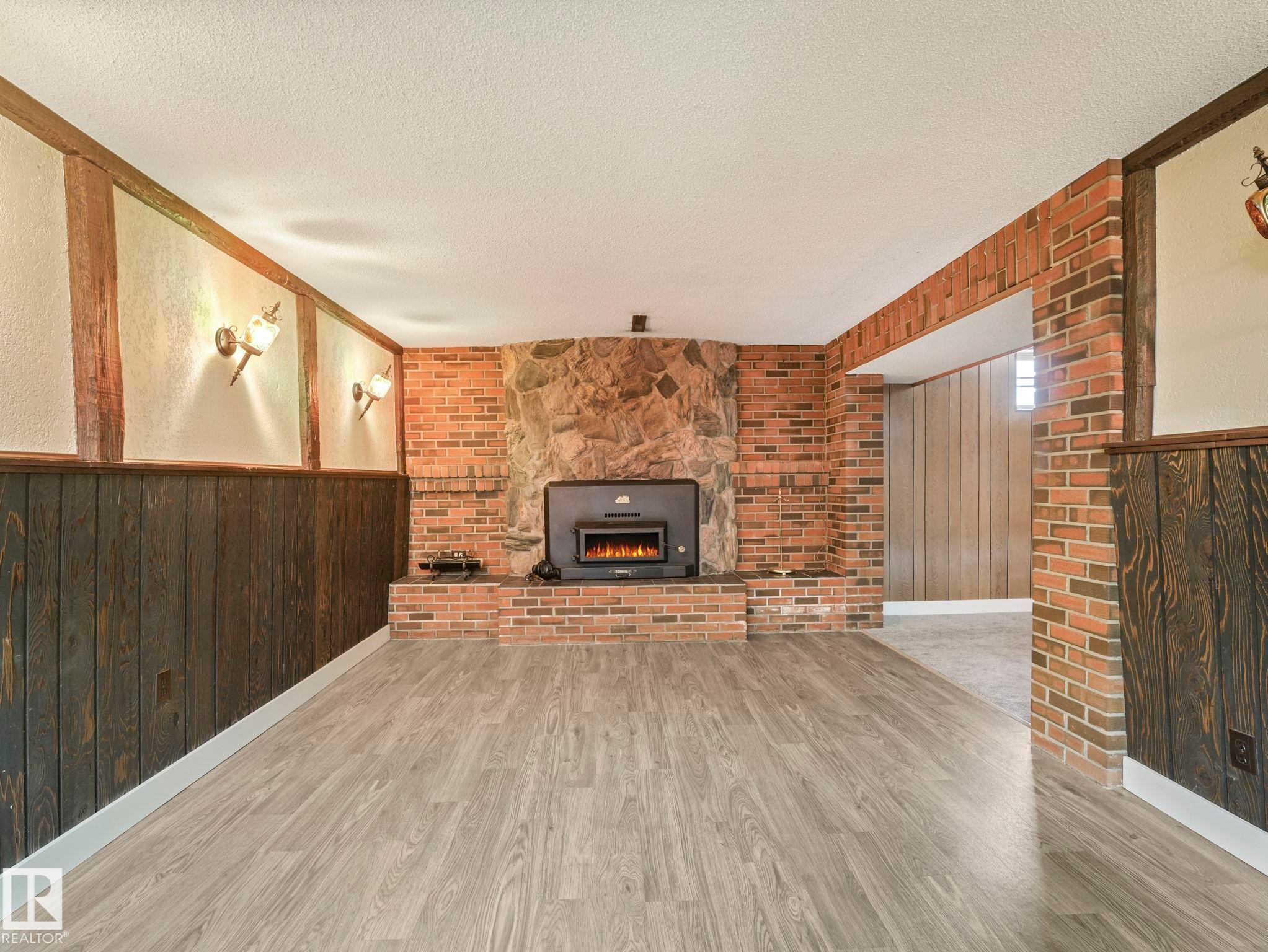 Living area featuring light-colored flooring, exposed brick, and a stone fireplace with a wood-burning insert - 5904 84 Avenue, Edmonton, AB - Indoor With Fireplace