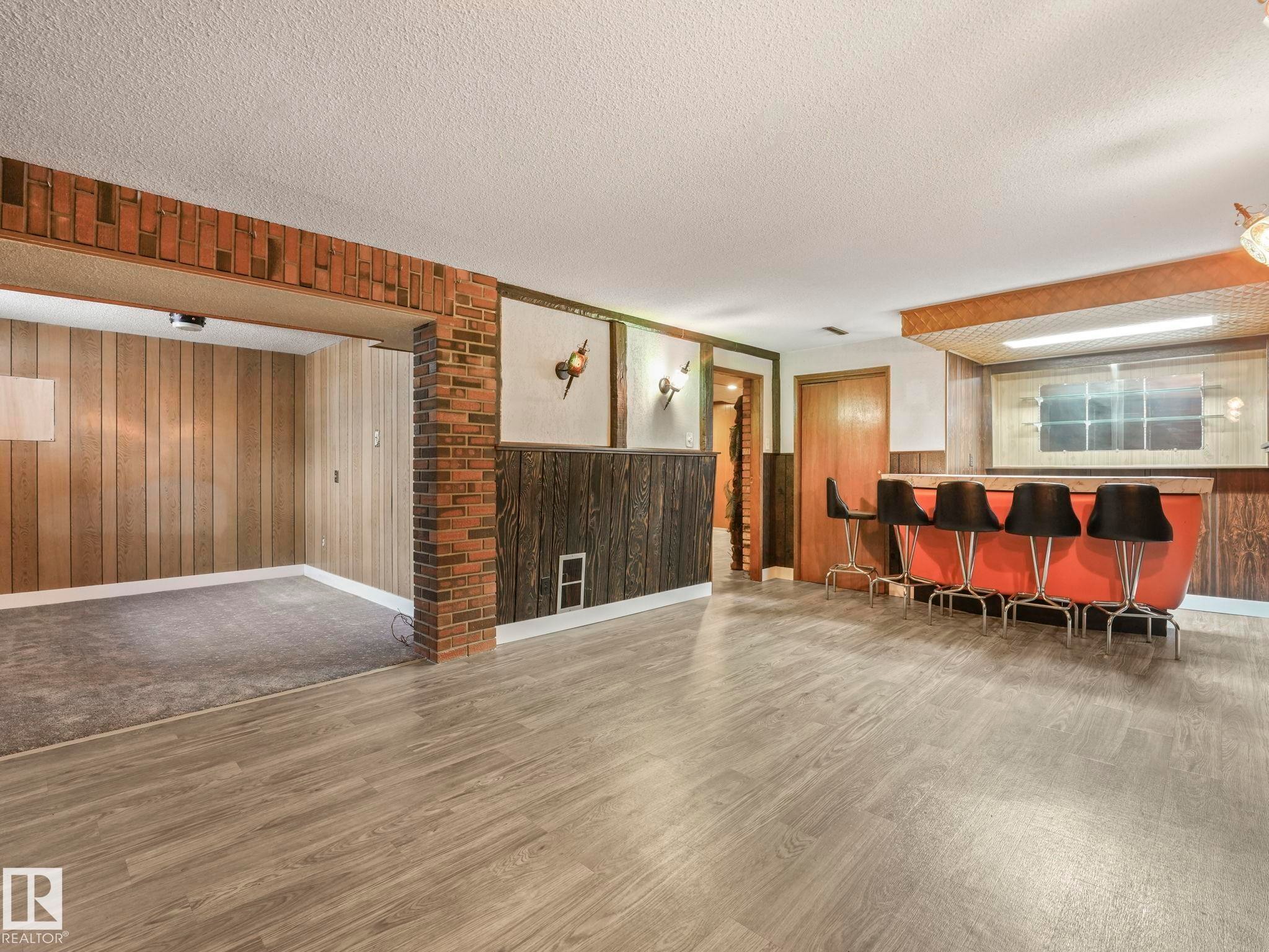 This expansive room features light-toned flooring, brick accents, and wood paneling on the walls - 5904 84 Avenue, Edmonton, AB - Indoor