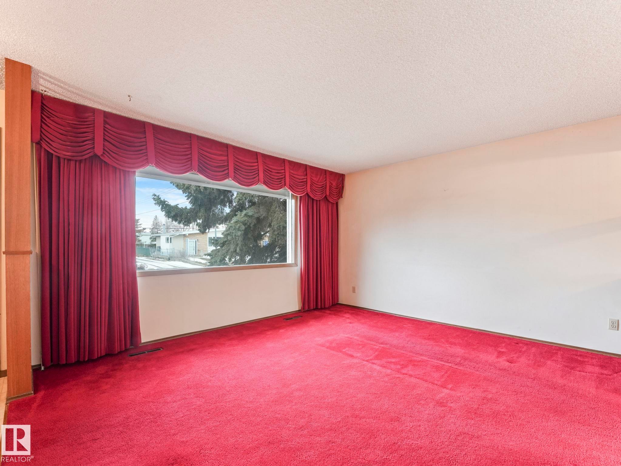 The property features a spacious room with wall-to-wall carpeting, a large window providing ample natural light, and elegant red drapery with a valance - 5904 84 Avenue, Edmonton, AB - Indoor Photo Showing Other Room