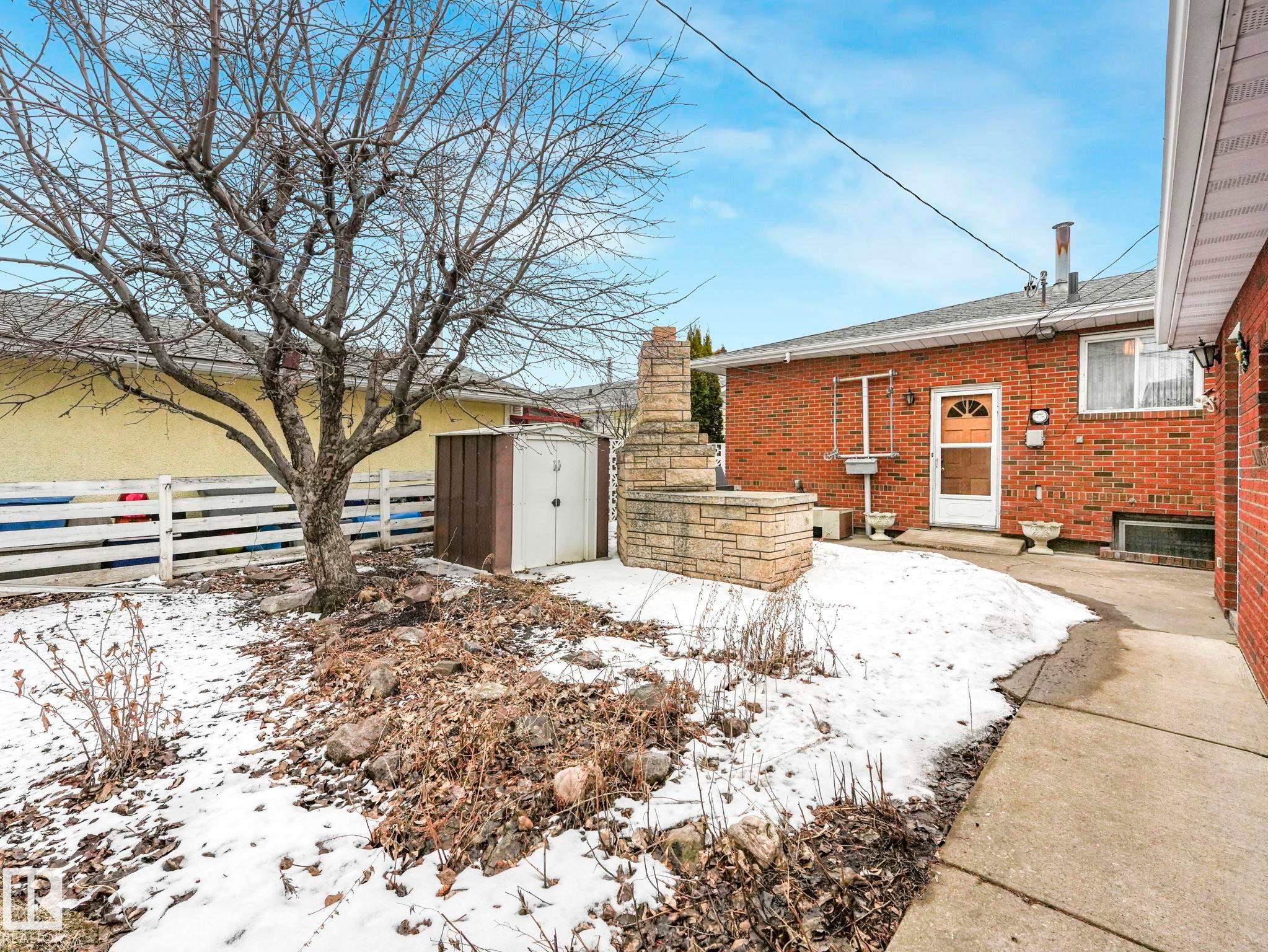 The property features a brick exterior, a paved walkway, and a stone planter with a chimney structure - 5904 84 Avenue, Edmonton, AB - Outdoor
