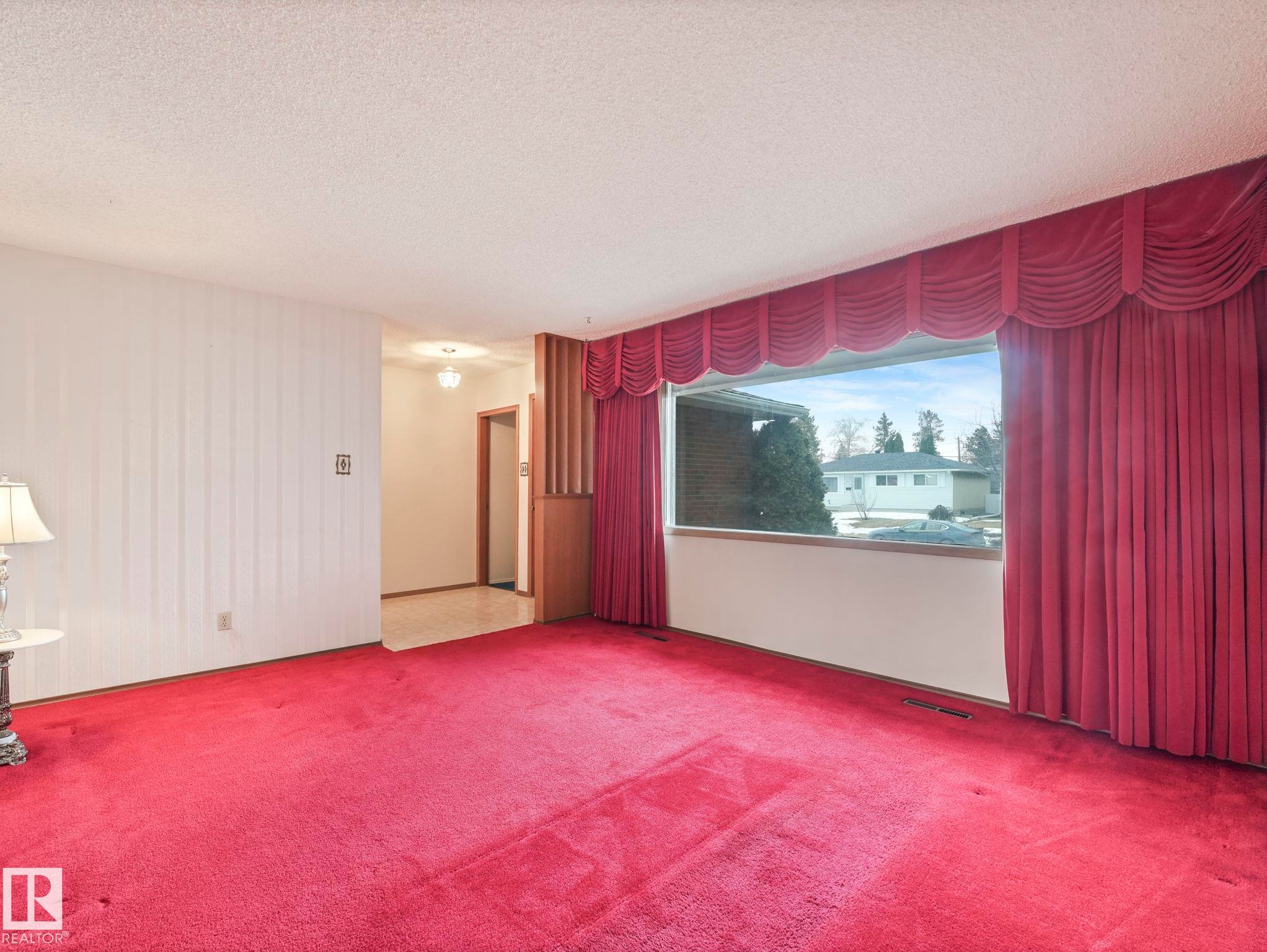 The living area features a large window with drapes, carpeting, and light-colored walls - 5904 84 Avenue, Edmonton, AB - Indoor Photo Showing Other Room