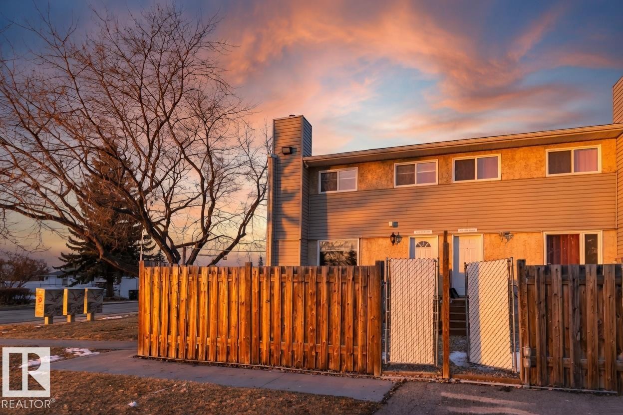 The property features a two-story exterior with horizontal siding and stucco finishes, framed by a wooden fence with white gates - 8620 38A Avenue, Edmonton, AB - Outdoor