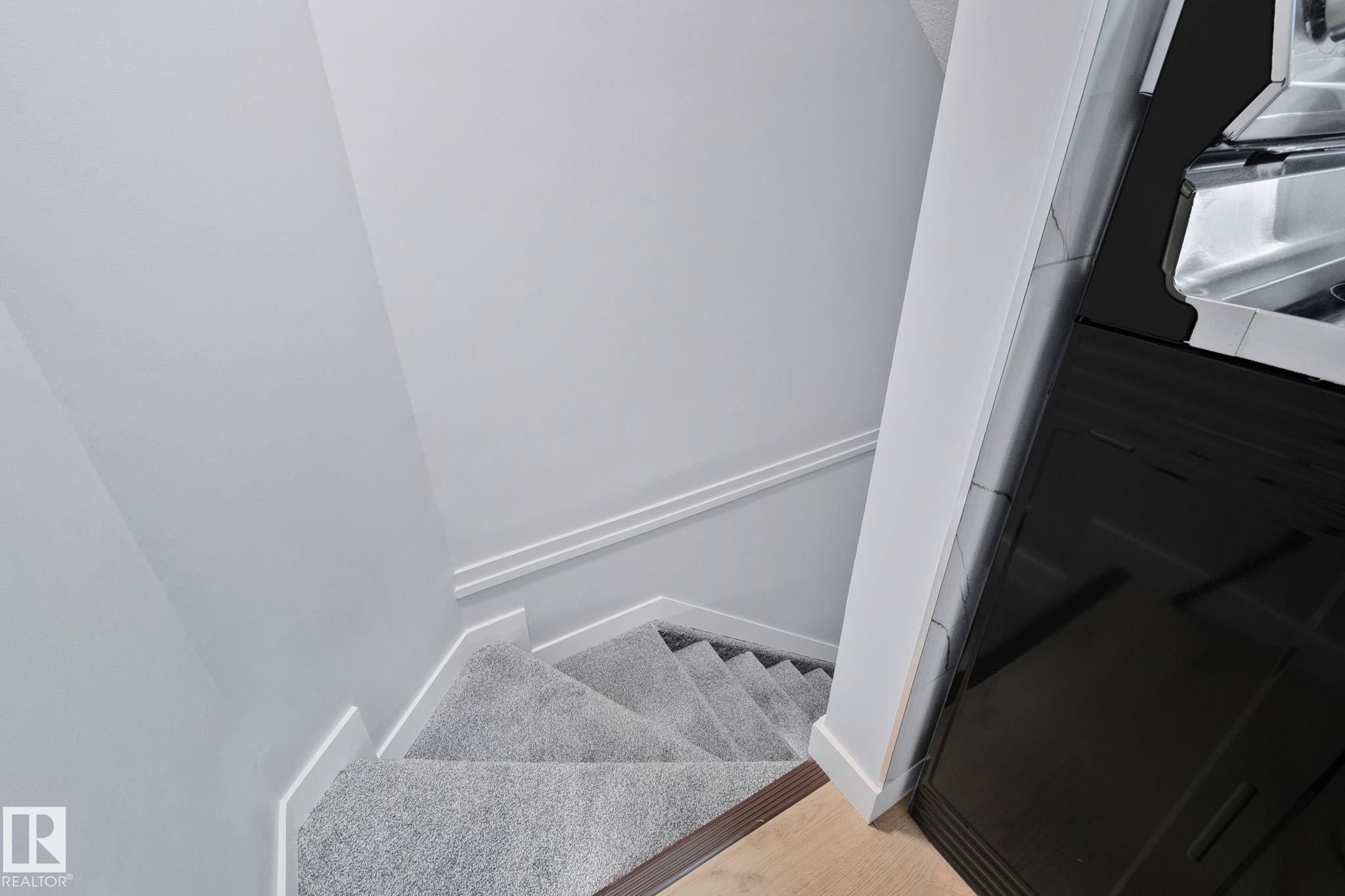 The property features a staircase with light grey carpeting, white baseboards, and a light-colored wall - 8620 38A Avenue, Edmonton, AB - Indoor Photo Showing Other Room