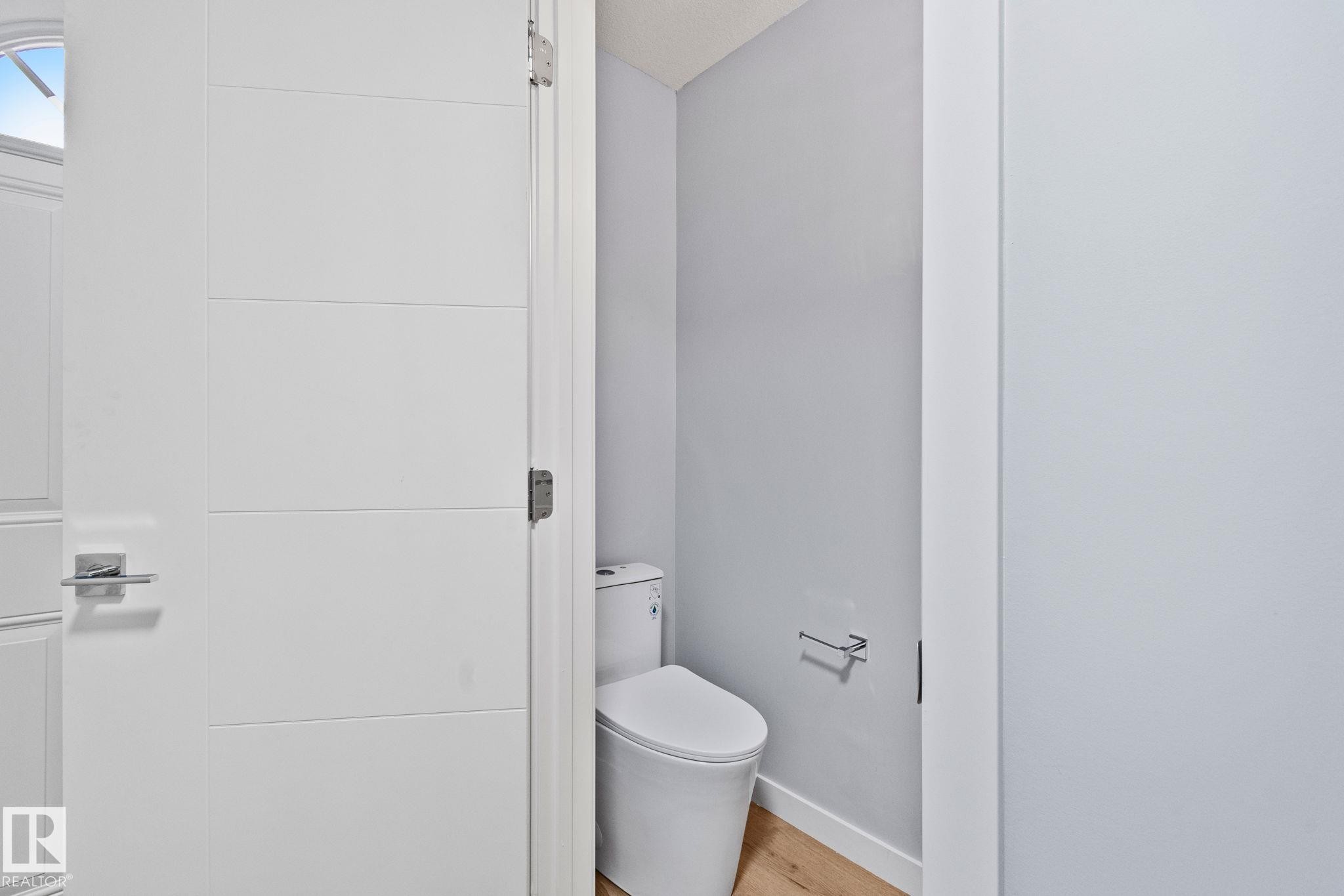 Bathroom featuring light gray walls, light hardwood flooring, and a modern white toilet - 8620 38A Avenue, Edmonton, AB - Indoor Photo Showing Bathroom