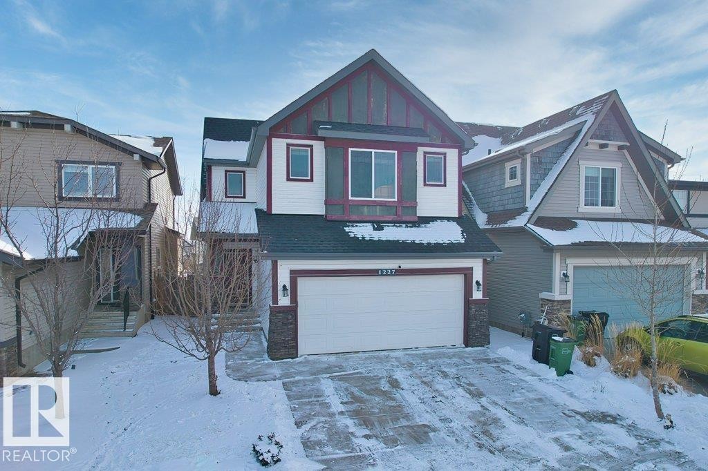 The property features a white exterior with dark red trim, a dark gray roof, and stone accents - 1227 Secord Landing, Edmonton, AB - Outdoor With Facade
