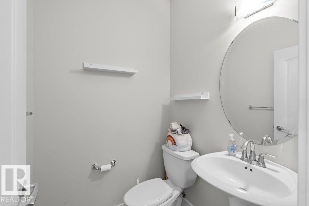 The bathroom features a pedestal sink with a chrome faucet, an oval mirror, and a toilet - 1227 Secord Landing, Edmonton, AB - Indoor Photo Showing Bathroom