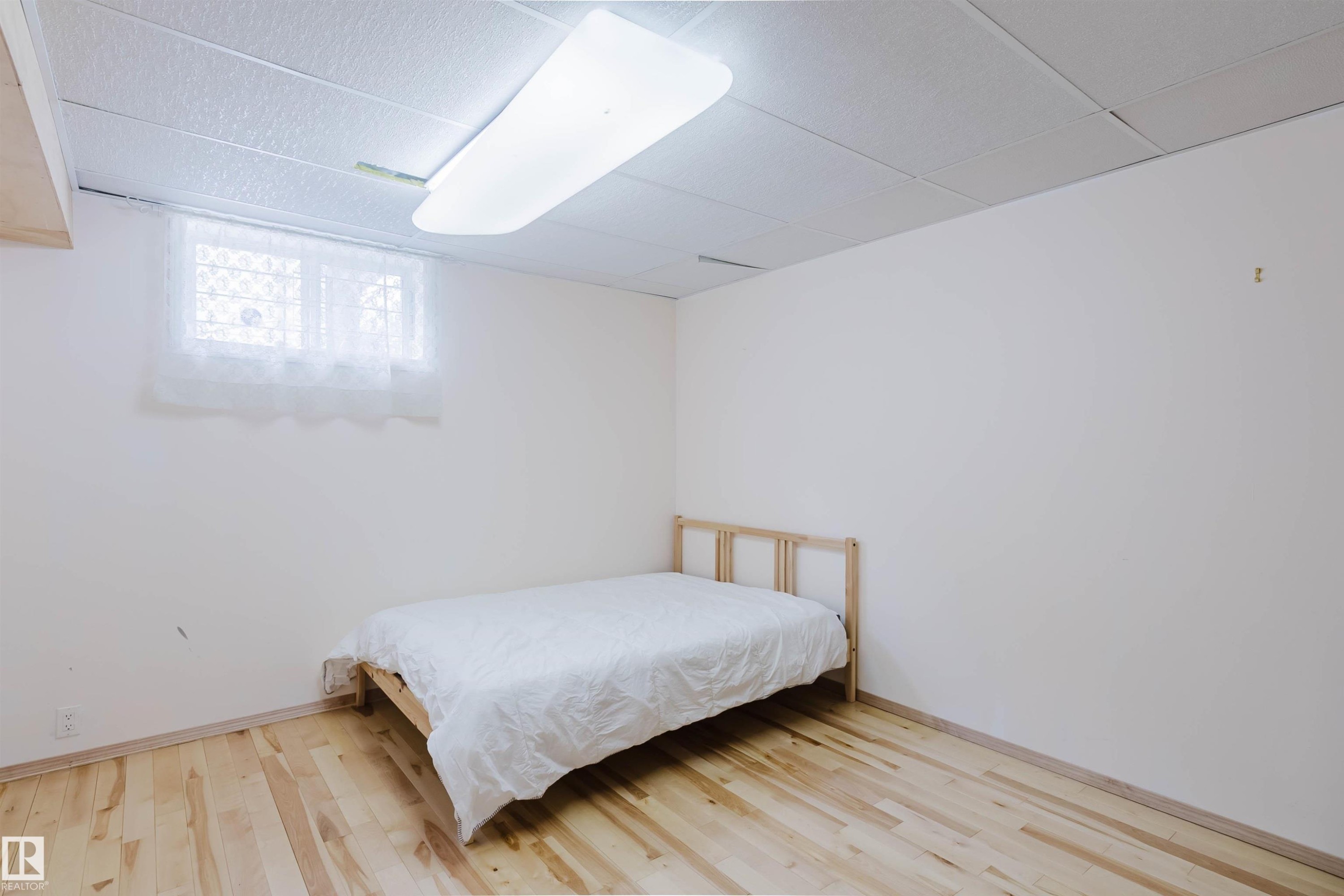 Room featuring light wood flooring, white walls, and a window with white curtains - 11815 76 Avenue, Edmonton, AB - Indoor Photo Showing Bedroom