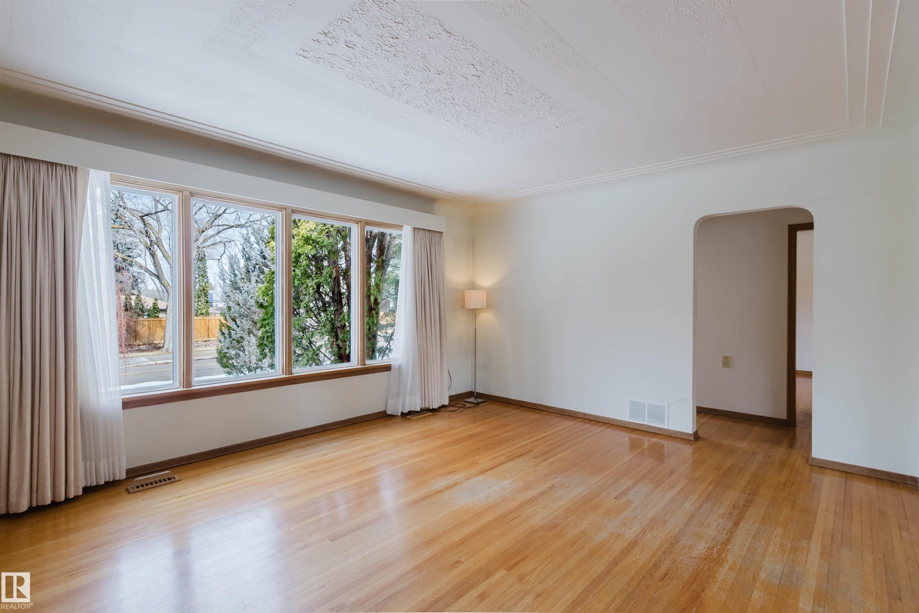 This room features polished hardwood floors, a large picture window with a garden view, and a decorative ceiling - 11815 76 Avenue, Edmonton, AB - Indoor Photo Showing Other Room