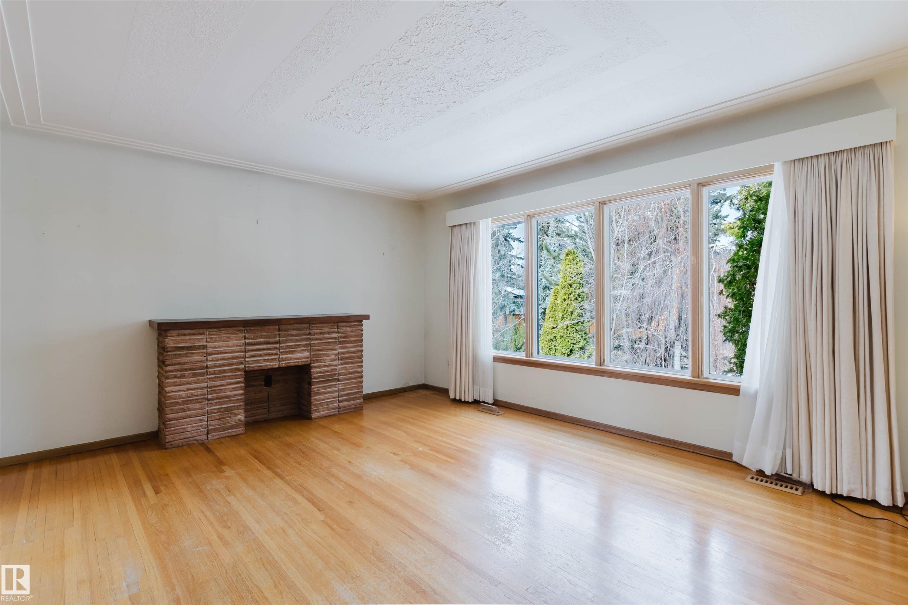 This room features hardwood floors, a brick fireplace, and large windows providing views of the outdoors - 11815 76 Avenue, Edmonton, AB - Indoor With Fireplace
