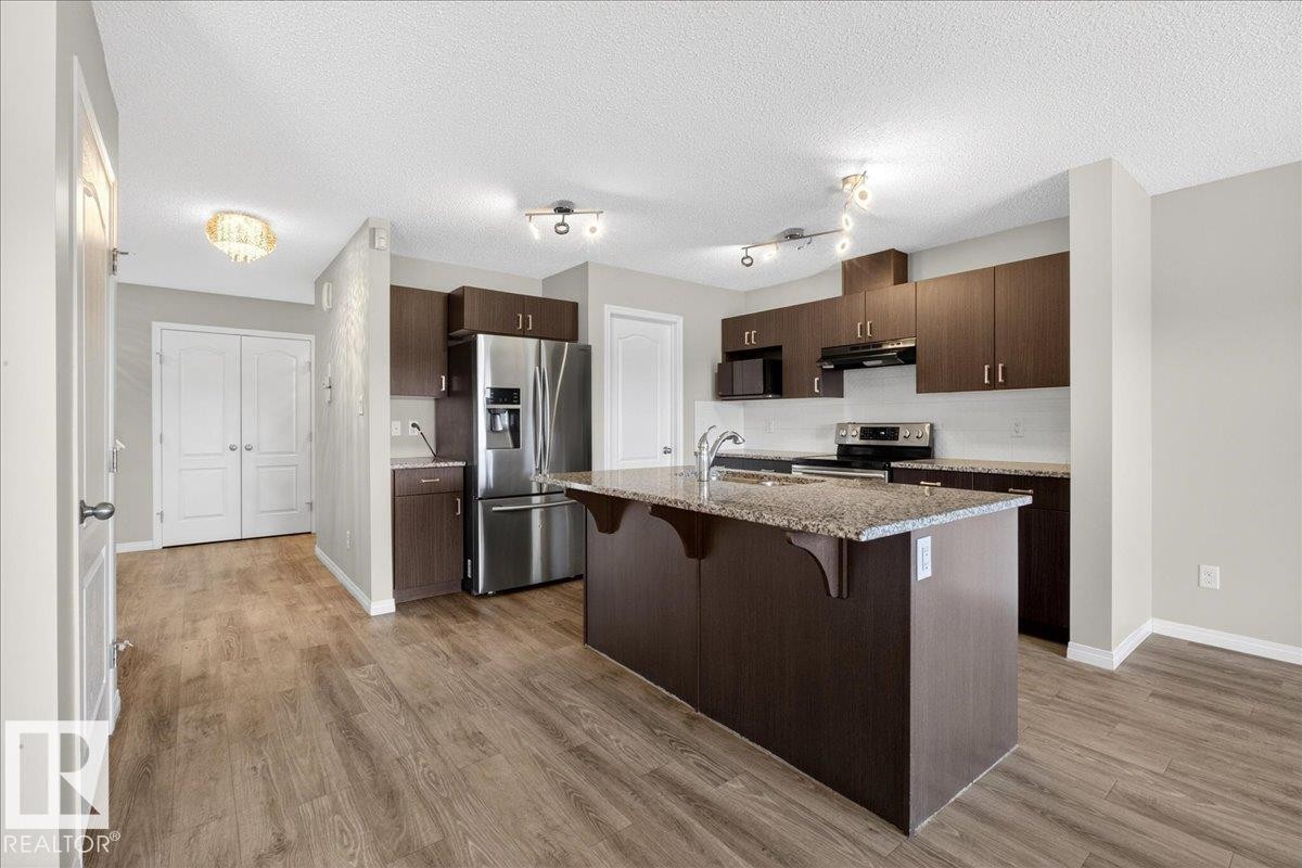 The property features a kitchen with dark cabinetry, stainless steel appliances, and a central island with a granite countertop - 17023 38 Street Nw, Edmonton, AB - Indoor Photo Showing Kitchen