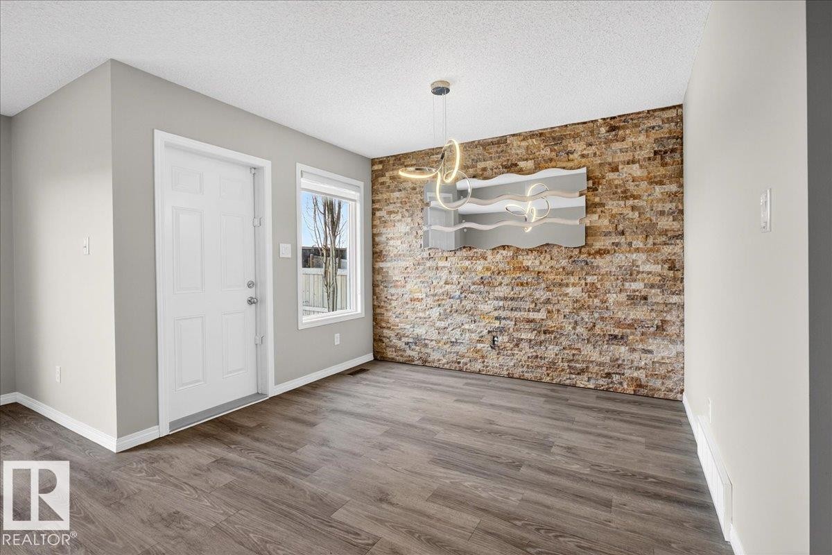 The property features hardwood style flooring, a stone accent wall, and a modern light fixture - 17023 38 Street Nw, Edmonton, AB - Indoor Photo Showing Other Room