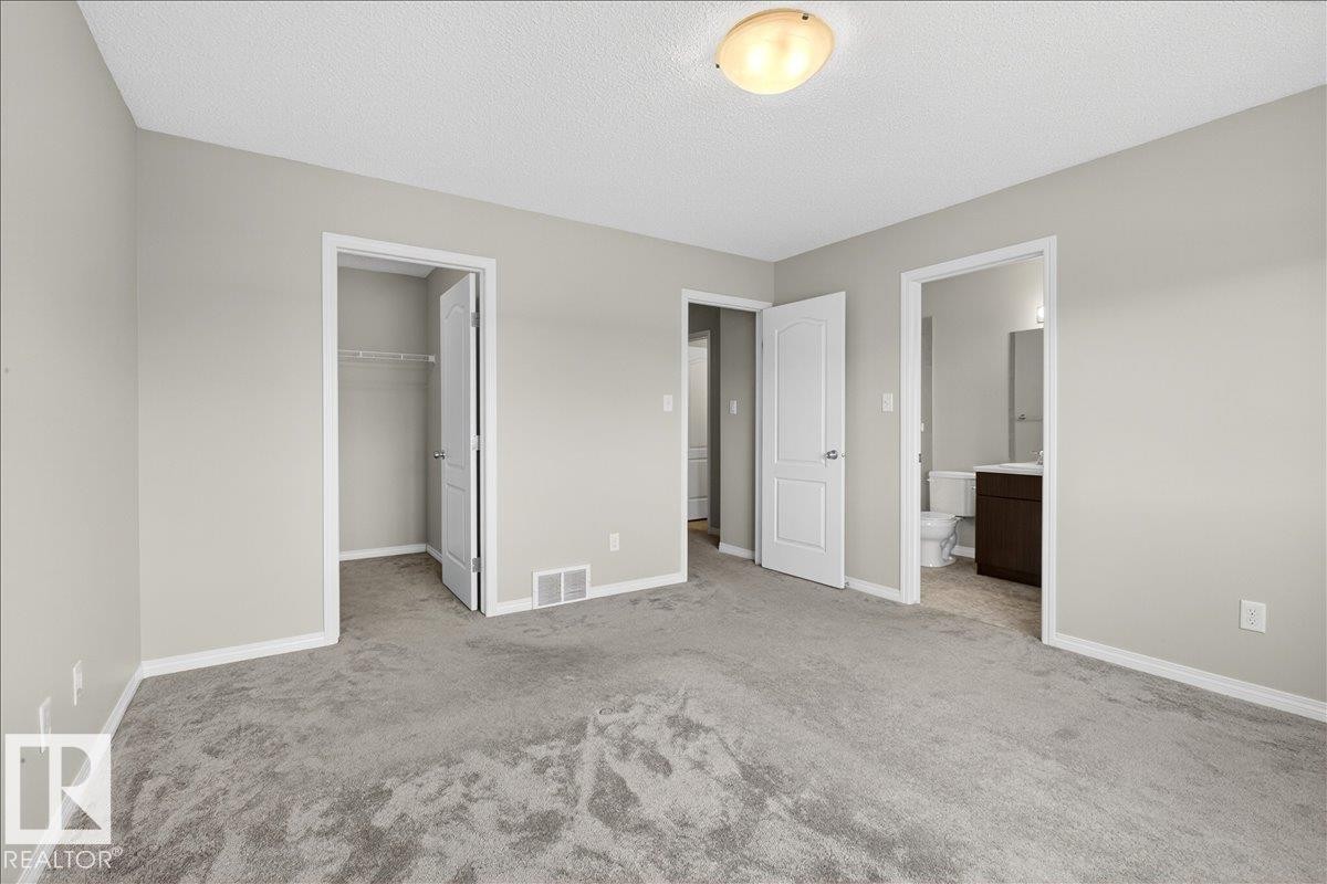 This bedroom features light grey carpeting, light grey painted walls, and white trim throughout. With in-suite bathroom and walk-in closet - 17023 38 Street Nw, Edmonton, AB - Indoor