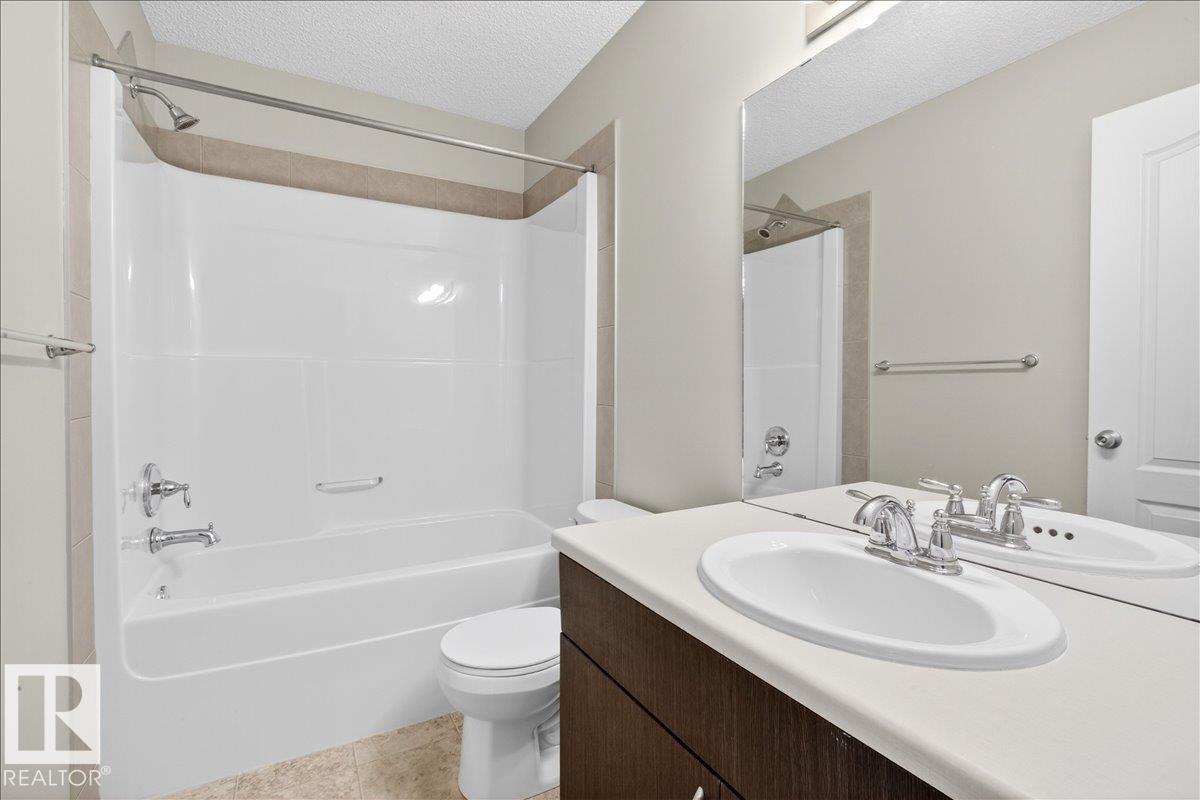 The bathroom features a vanity with an integrated sink and chrome faucet, a large mirror, and a bathtub with a shower - 17023 38 Street Nw, Edmonton, AB - Indoor Photo Showing Bathroom
