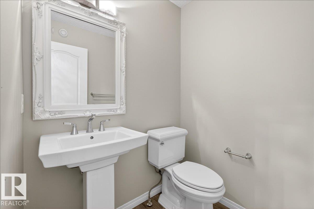 This bathroom features a white pedestal sink with a chrome faucet, a toilet, and a decorative white framed mirror - 17023 38 Street Nw, Edmonton, AB - Indoor Photo Showing Bathroom
