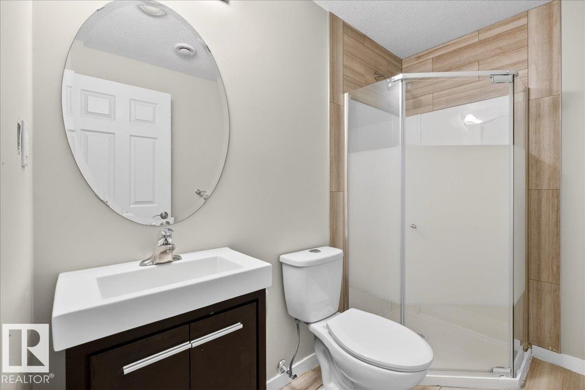This basement bathroom features a contemporary vanity with an integrated sink and an oval mirror, alongside a standing shower with a glass enclosure and tiled walls - 17023 38 Street Nw, Edmonton, AB - Indoor Photo Showing Bathroom