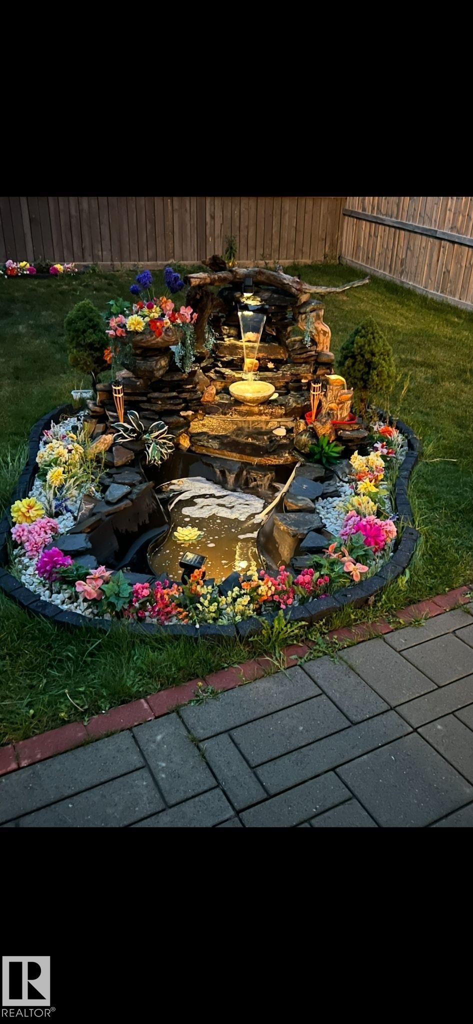 The property features an attractive outdoor water feature with integrated lighting, surrounded by varied plantings and decorative rocks - 17023 38 Street Nw, Edmonton, AB - Outdoor