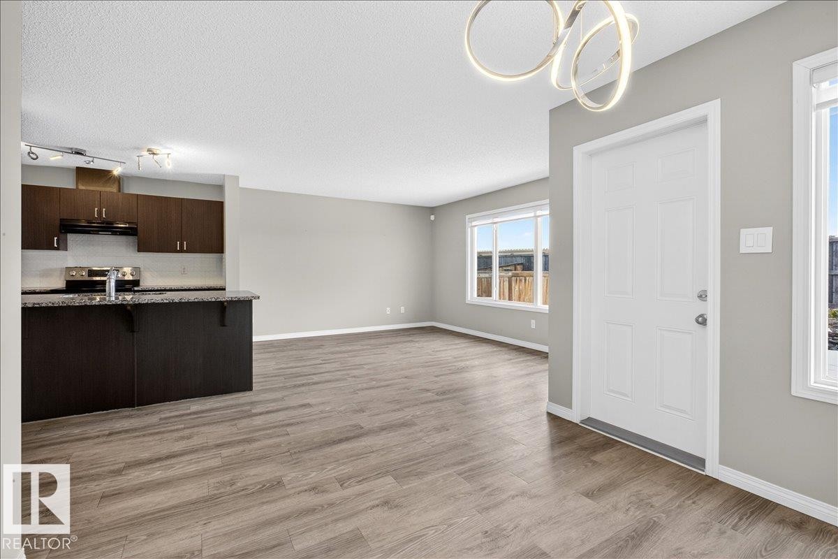The property features an open-concept living area with wood-look flooring and light gray walls - 17023 38 Street Nw, Edmonton, AB - Indoor Photo Showing Kitchen