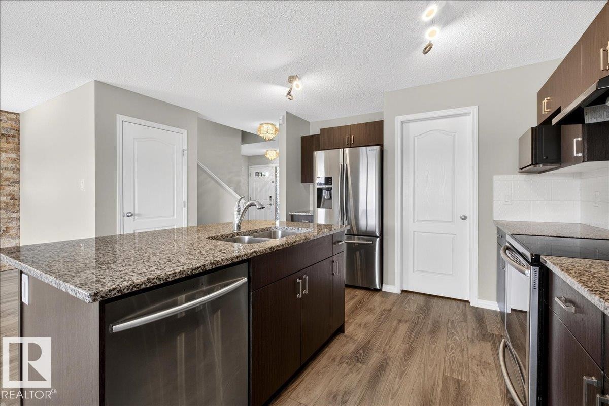 The kitchen features granite countertops, dark wood cabinetry, a double sink, and stainless steel appliances including a dishwasher and refrigerator - 17023 38 Street Nw, Edmonton, AB - Indoor Photo Showing Kitchen With Double Sink With Upgraded Kitchen