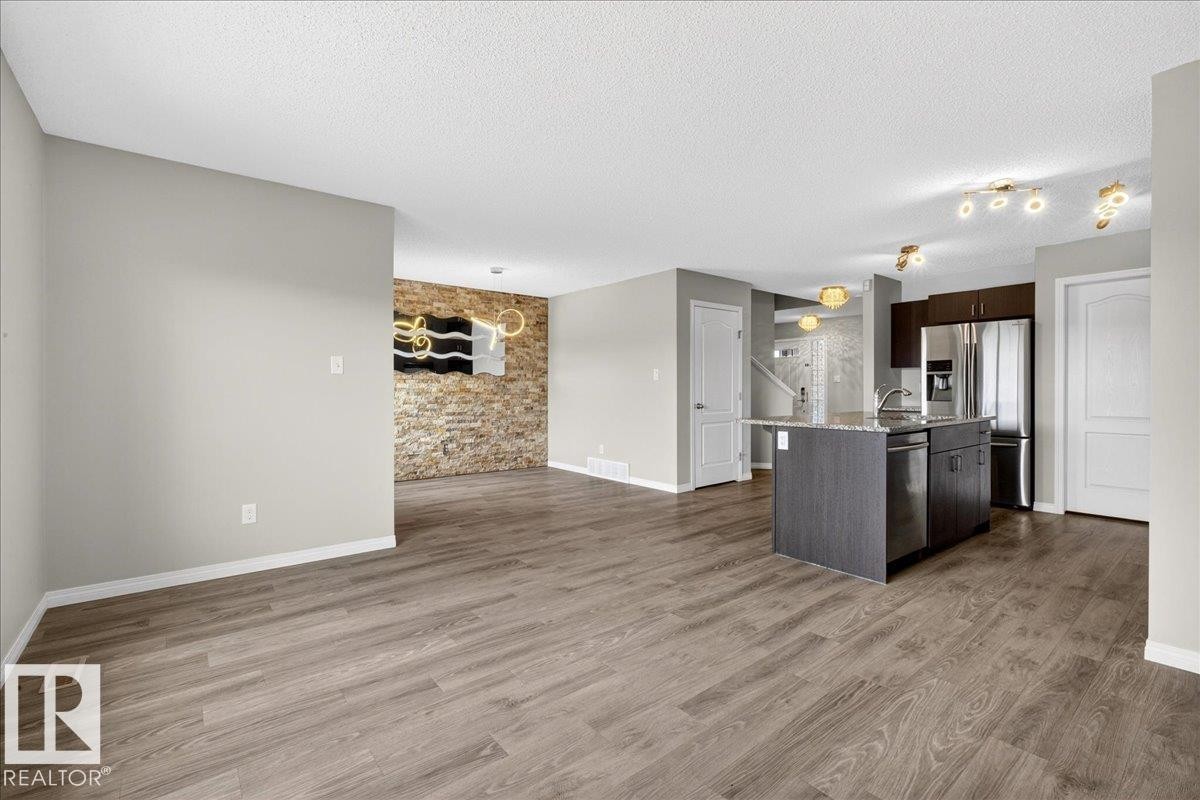 Open concept living area featuring wood-look flooring, a kitchen island with a granite countertop, and a stainless steel refrigerator - 17023 38 Street Nw, Edmonton, AB - Indoor Photo Showing Kitchen