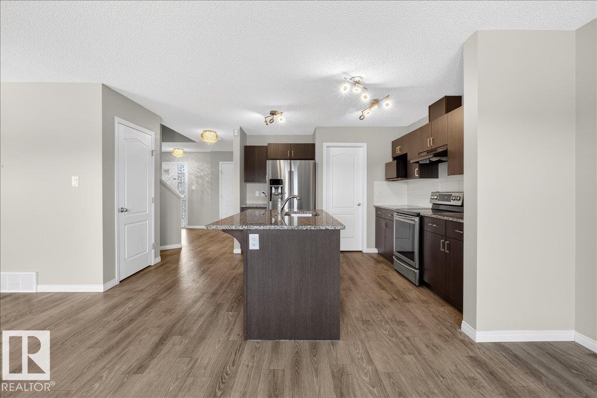 The kitchen features a central island with a granite countertop and an undermount sink, dark wood cabinetry, and stainless steel appliances - 17023 38 Street Nw, Edmonton, AB - Indoor Photo Showing Kitchen