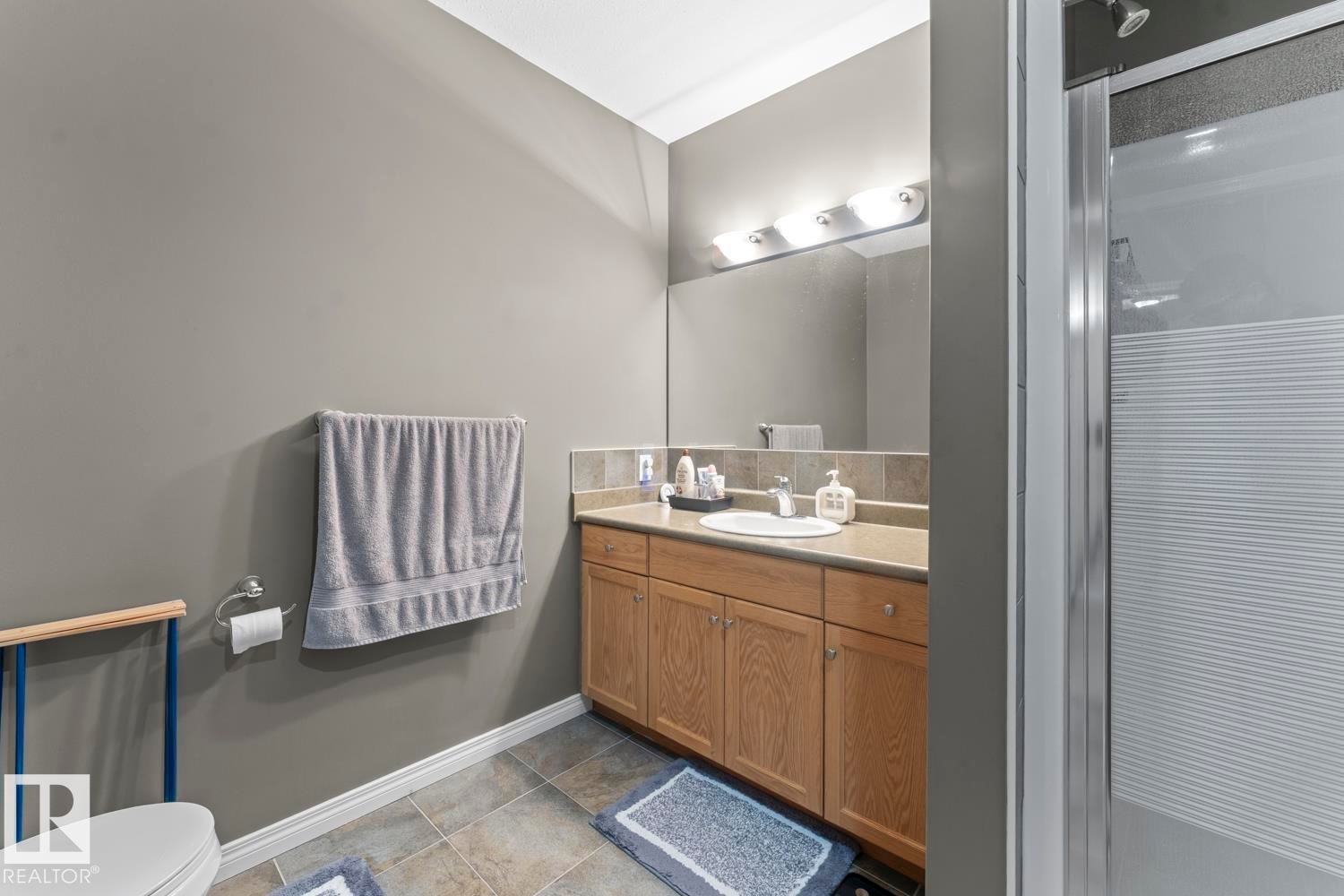 The bathroom features a vanity with light wood cabinetry and a large mirror, alongside a shower with a glass enclosure - 107 801 11 Street, Cold Lake, AB - Indoor Photo Showing Bathroom