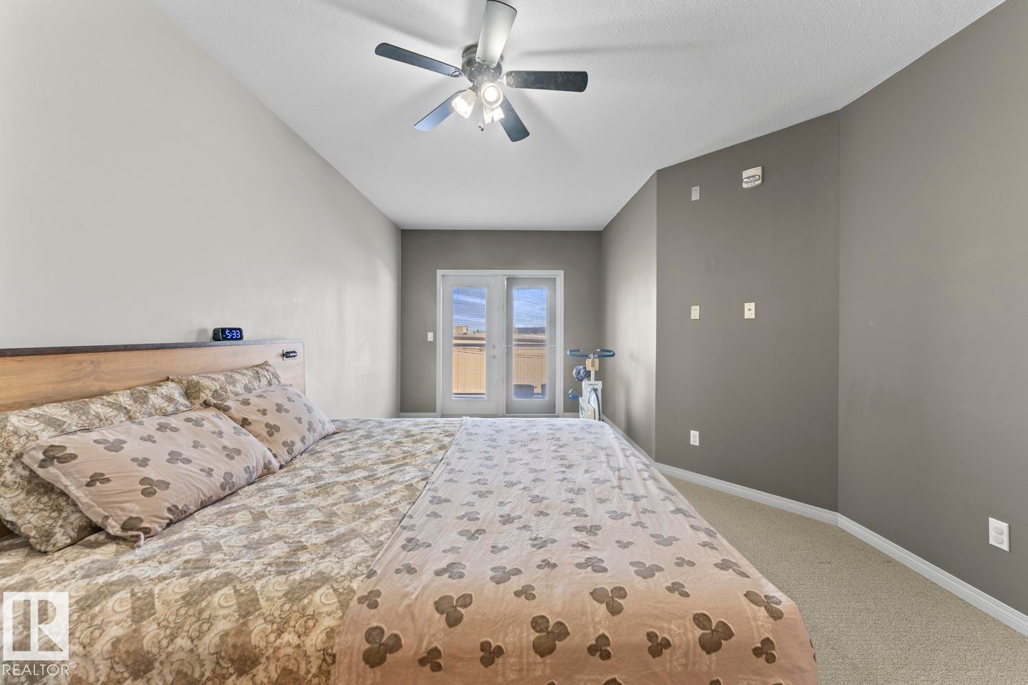 This room features a vaulted ceiling with a ceiling fan, carpeted flooring, and a set of double glass doors - 107 801 11 Street, Cold Lake, AB - Indoor Photo Showing Bedroom