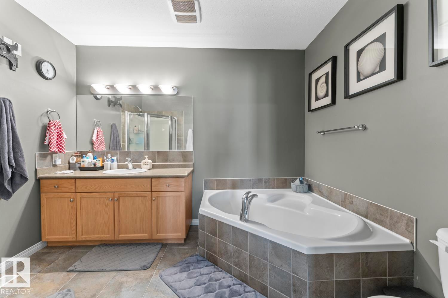 Bathroom featuring a vanity with a single sink, a large mirror, and a corner bathtub with tiled surround - 107 801 11 Street, Cold Lake, AB - Indoor Photo Showing Bathroom