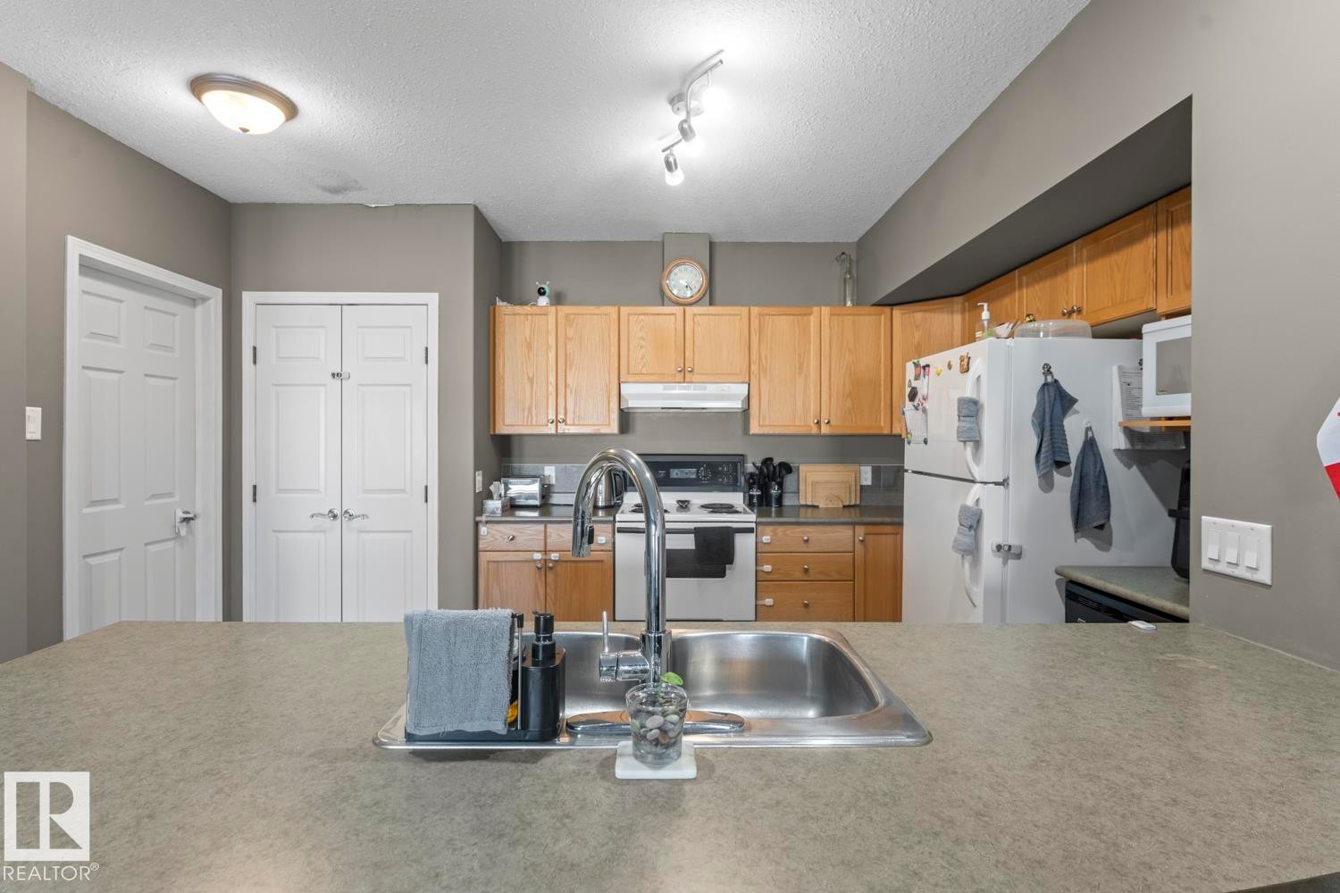The kitchen features light wood cabinetry, a stainless steel sink with a high arc faucet, and a range with a microwave above it - 107 801 11 Street, Cold Lake, AB - Indoor Photo Showing Kitchen