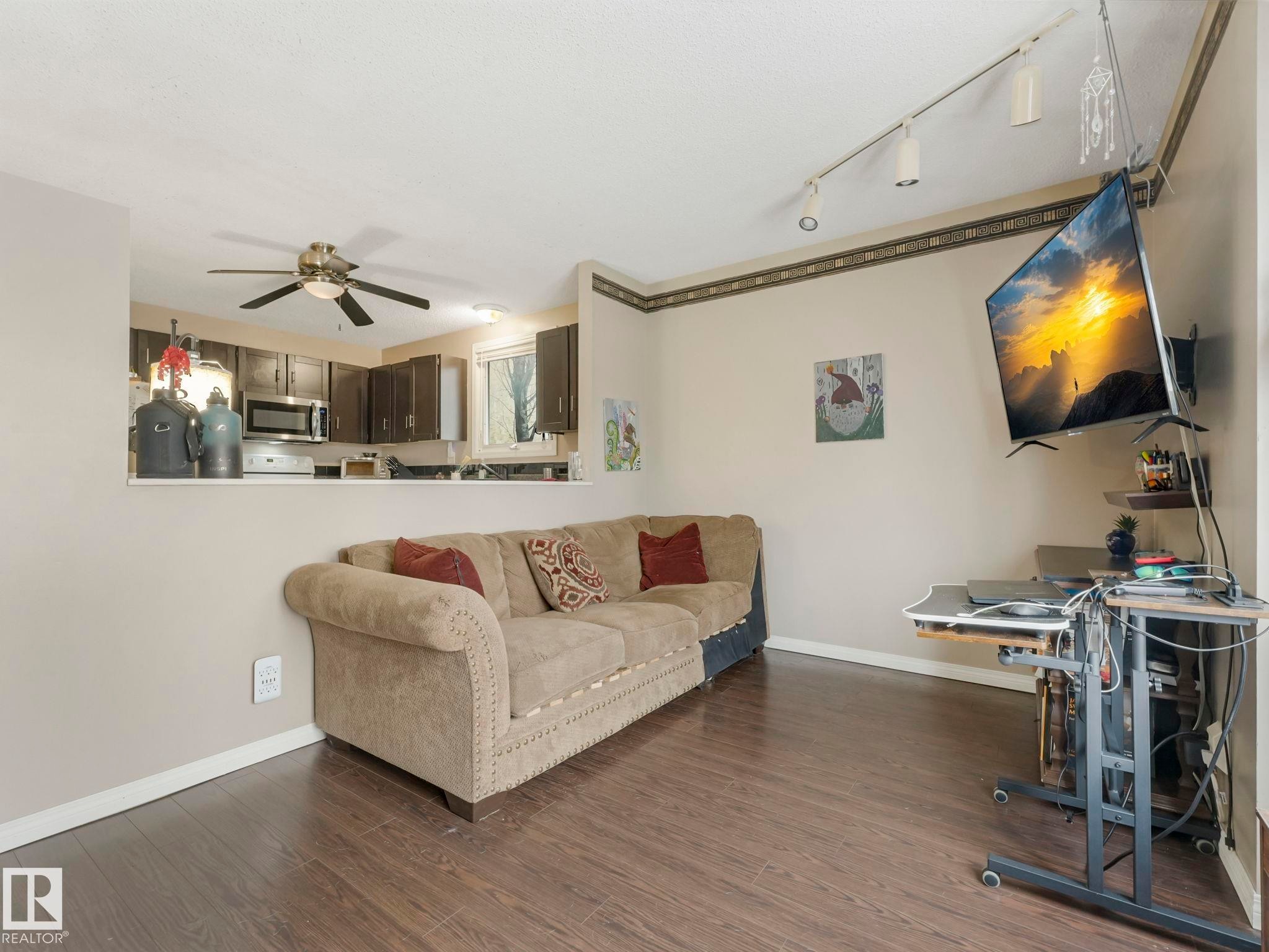 Living area featuring dark wood-style flooring, a light-colored wall with decorative trim, and track lighting - 4105 41 Avenue, Edmonton, AB - Indoor