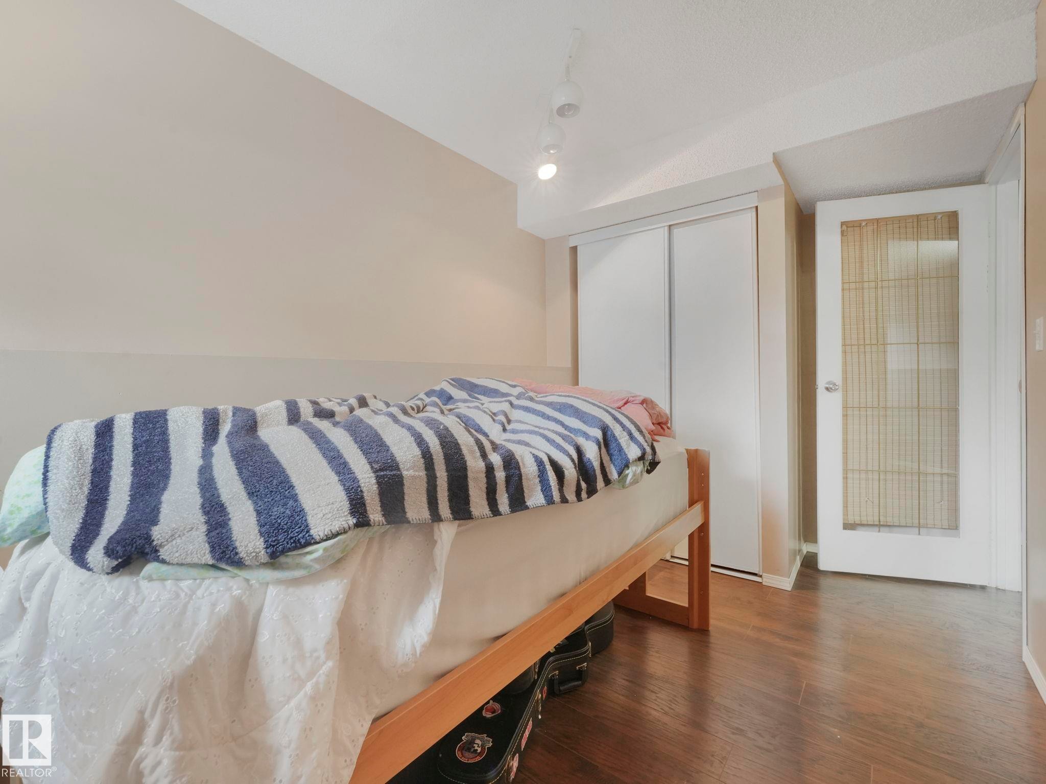 The room features wood flooring, a built-in closet with sliding doors, and a door with a frosted glass panel - 4105 41 Avenue, Edmonton, AB - Indoor Photo Showing Bedroom