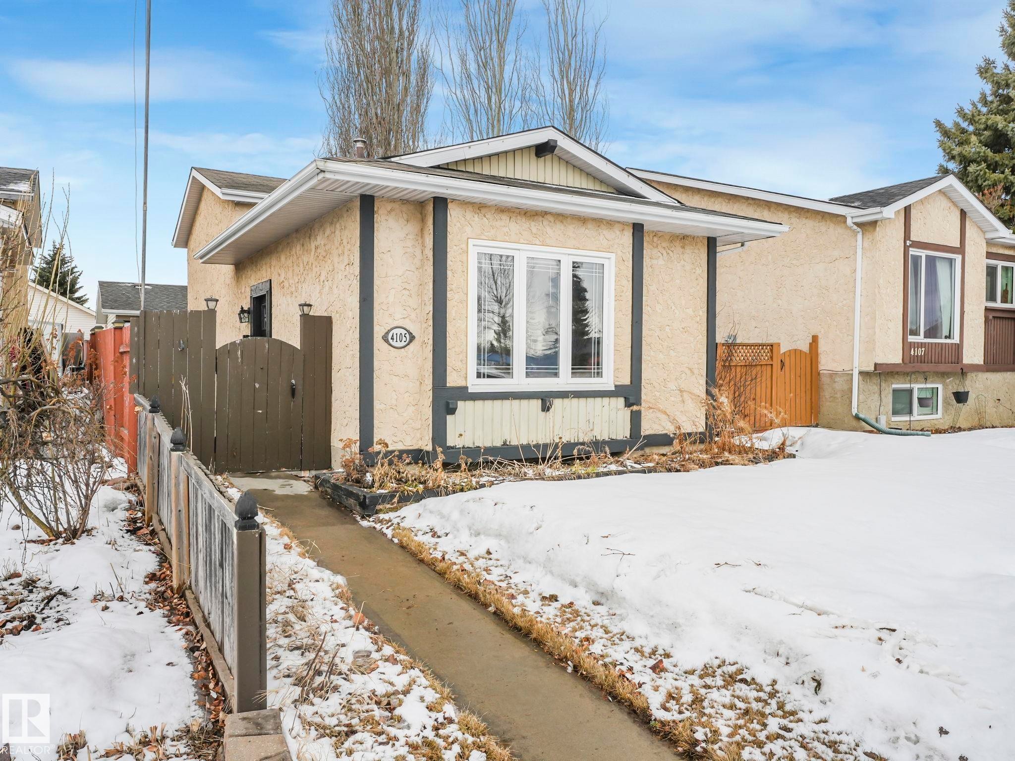 The property features a stucco exterior, a fenced yard, and a paved walkway leading to the entrance - 4105 41 Avenue, Edmonton, AB - Outdoor