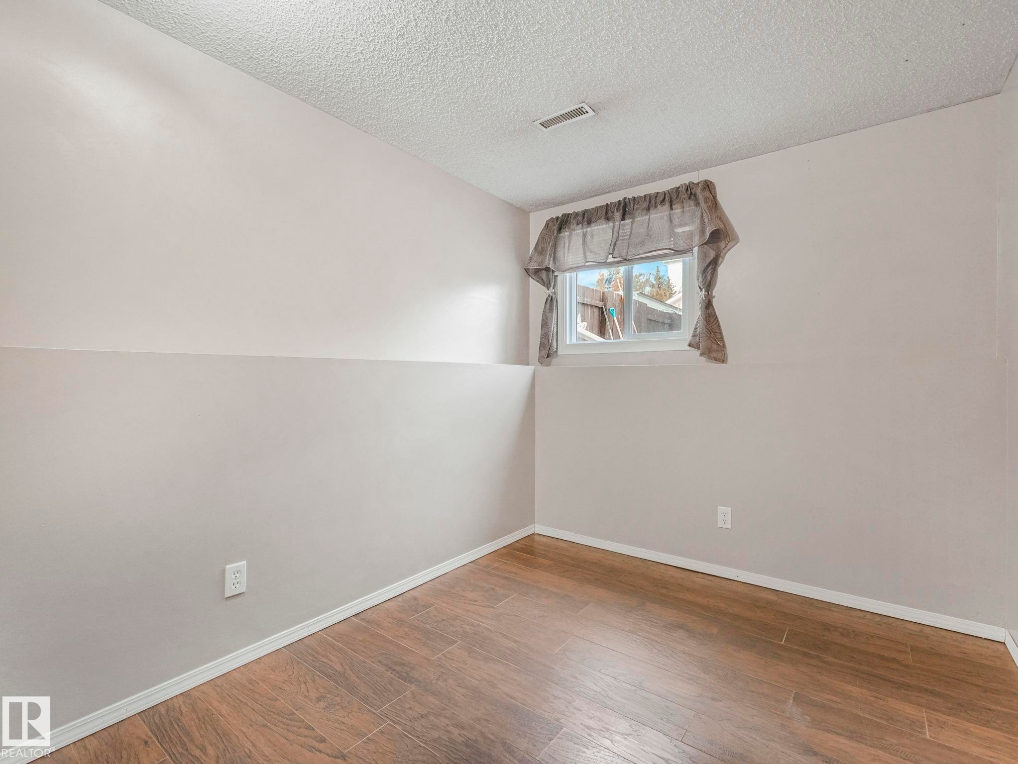 This room features wood-look flooring, light-toned walls, and a window with a valance - 4105 41 Avenue, Edmonton, AB - Indoor Photo Showing Other Room