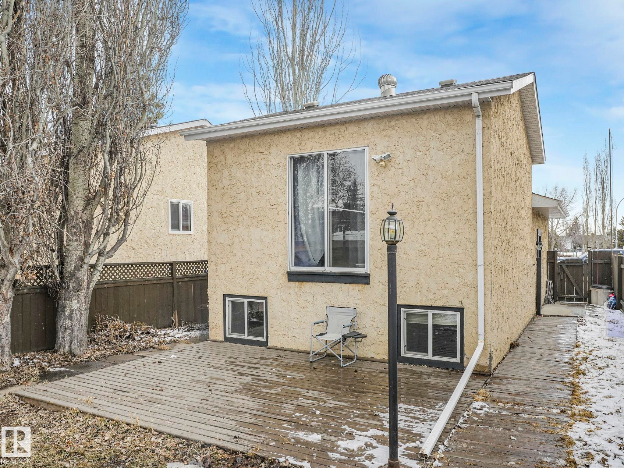 Rear exterior of the property featuring a wooden deck, stucco siding, and a large window - 4105 41 Avenue, Edmonton, AB - Outdoor With Exterior