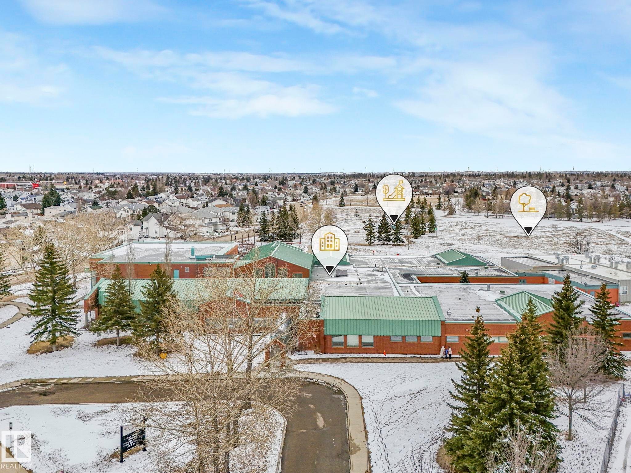 Aerial view showcasing the property's proximity to a large red brick building with a green roof, surrounded by evergreen trees and a snow-covered landscape - 4105 41 Avenue, Edmonton, AB - Outdoor With View