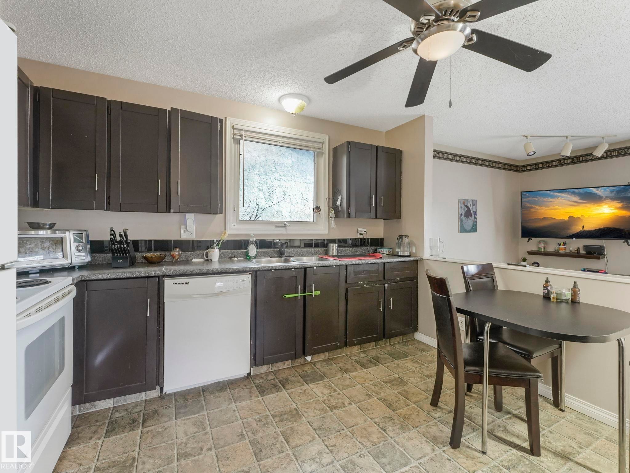 The kitchen features dark cabinetry, a white dishwasher, and a window above the sink - 4105 41 Avenue, Edmonton, AB - Indoor Photo Showing Kitchen