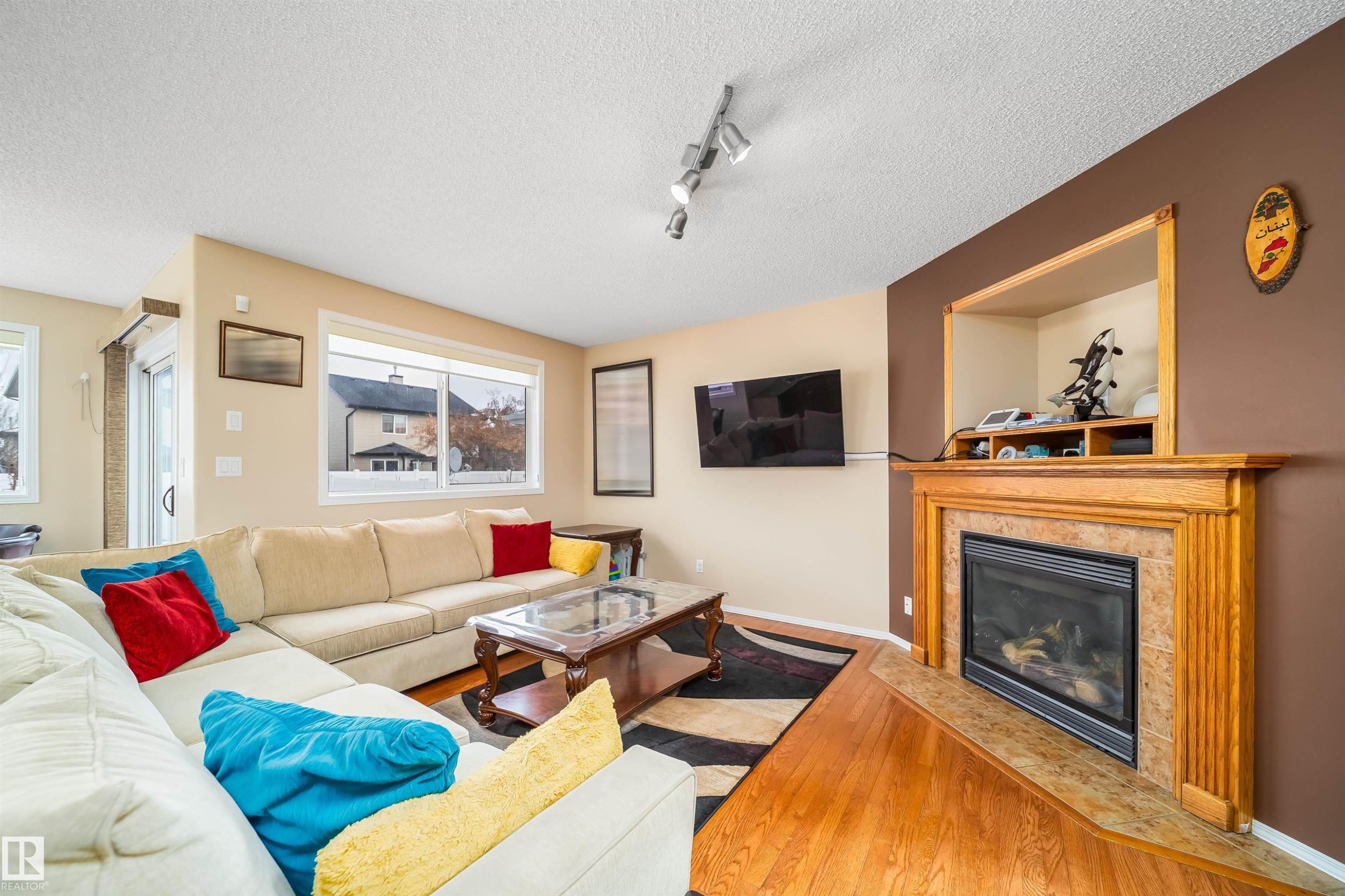 The living area features hardwood flooring, a fireplace with a natural wood mantel and stone surround, and windows that provide natural light - 8932 175 Avenue, Edmonton, AB - Indoor Photo Showing Living Room With Fireplace